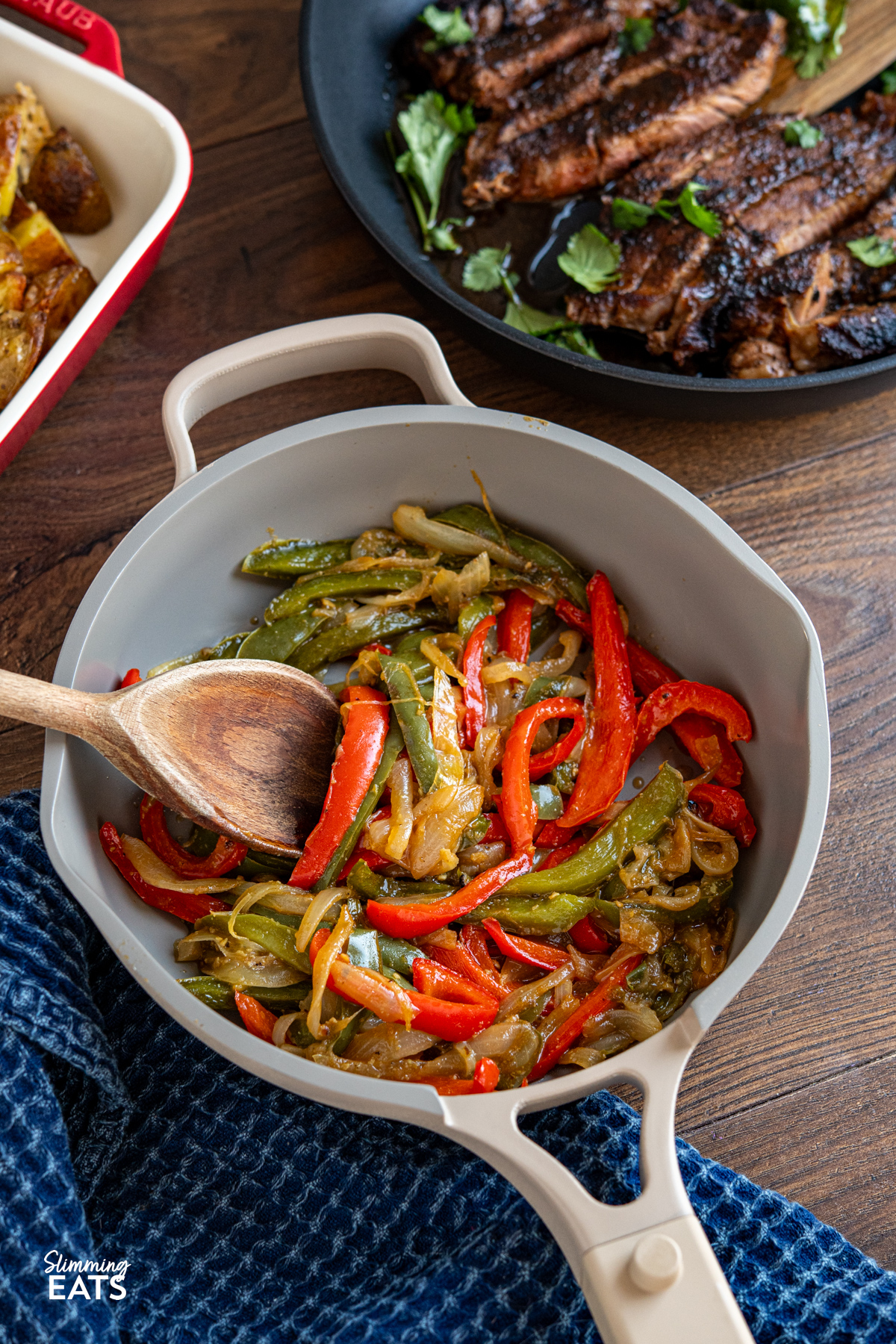 Simple, flavour packed sautéed peppers and onions cooked in stock for a tender, lightly caramelised side with minimal oil. Sauteed Peppers and Onions in a non stick frying pan with wooden spoon, sliced seasoned steak and peppers visible above