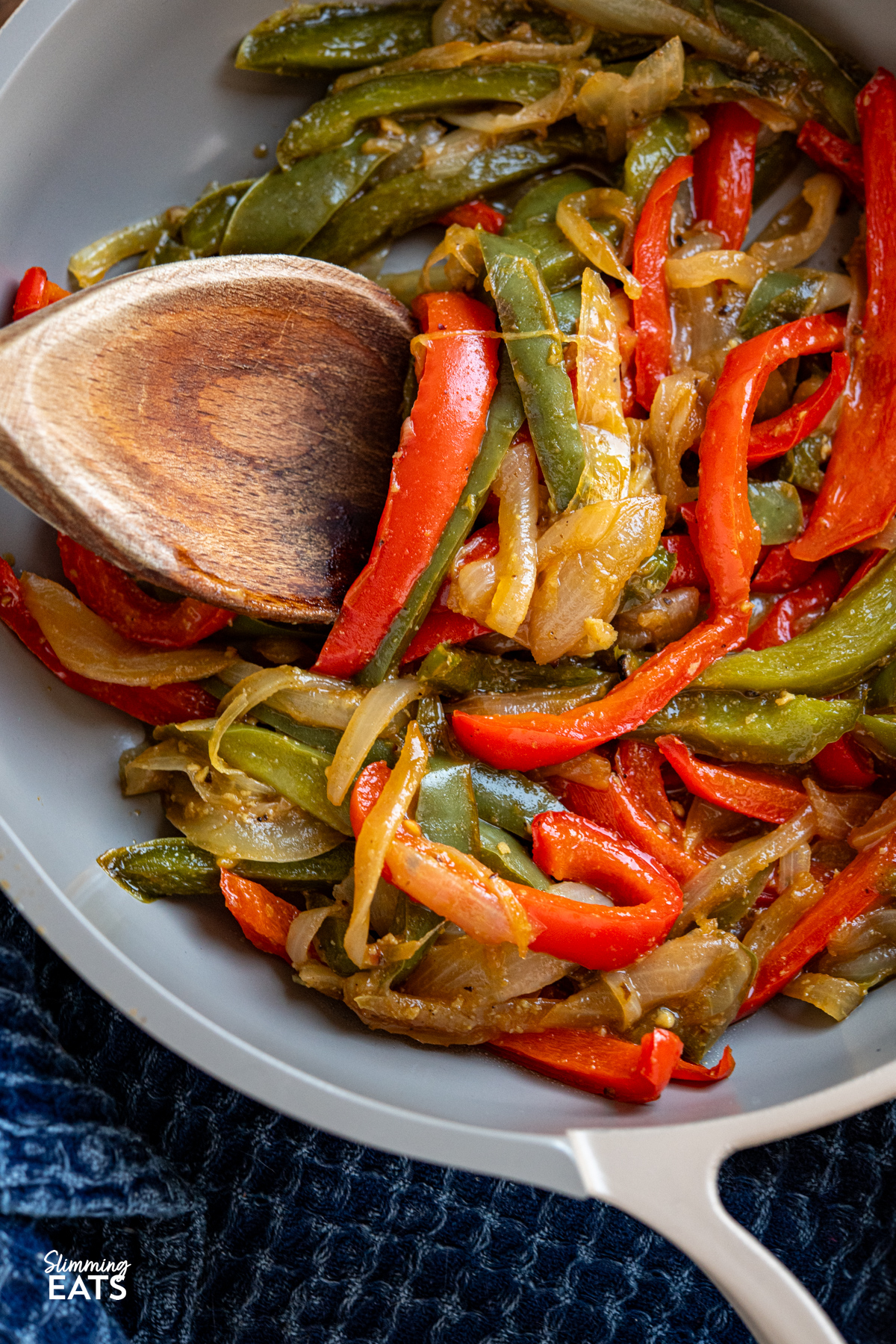 Simple, flavour packed sautéed peppers and onions cooked in stock for a tender, lightly caramelised side with minimal oil. close up of Sauteed Peppers and Onions in a non stick frying pan with wooden spoon