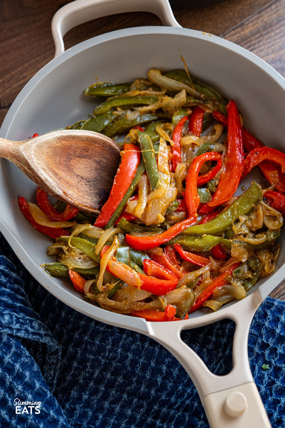 Simple, flavour packed sautéed peppers and onions cooked in stock for a tender, lightly caramelised side with minimal oil. close up of Sauteed Peppers and Onions in a non stick frying pan with wooden spoon