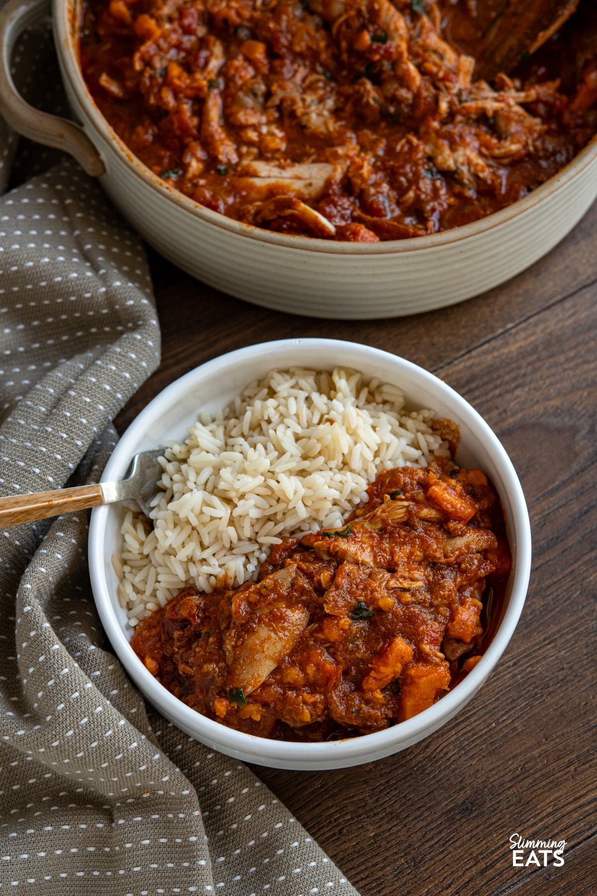 This Slow Cooker Chicken, Chorizo and Sweet Potato Stew is a hearty, flavour-packed meal that brings comfort and richness to any table. Slow Cooker Chicken Chorizo Sweet Potato Stew serving in a white bowl with long grain rice, ceramic double handled dish with the remaining stew visible above.