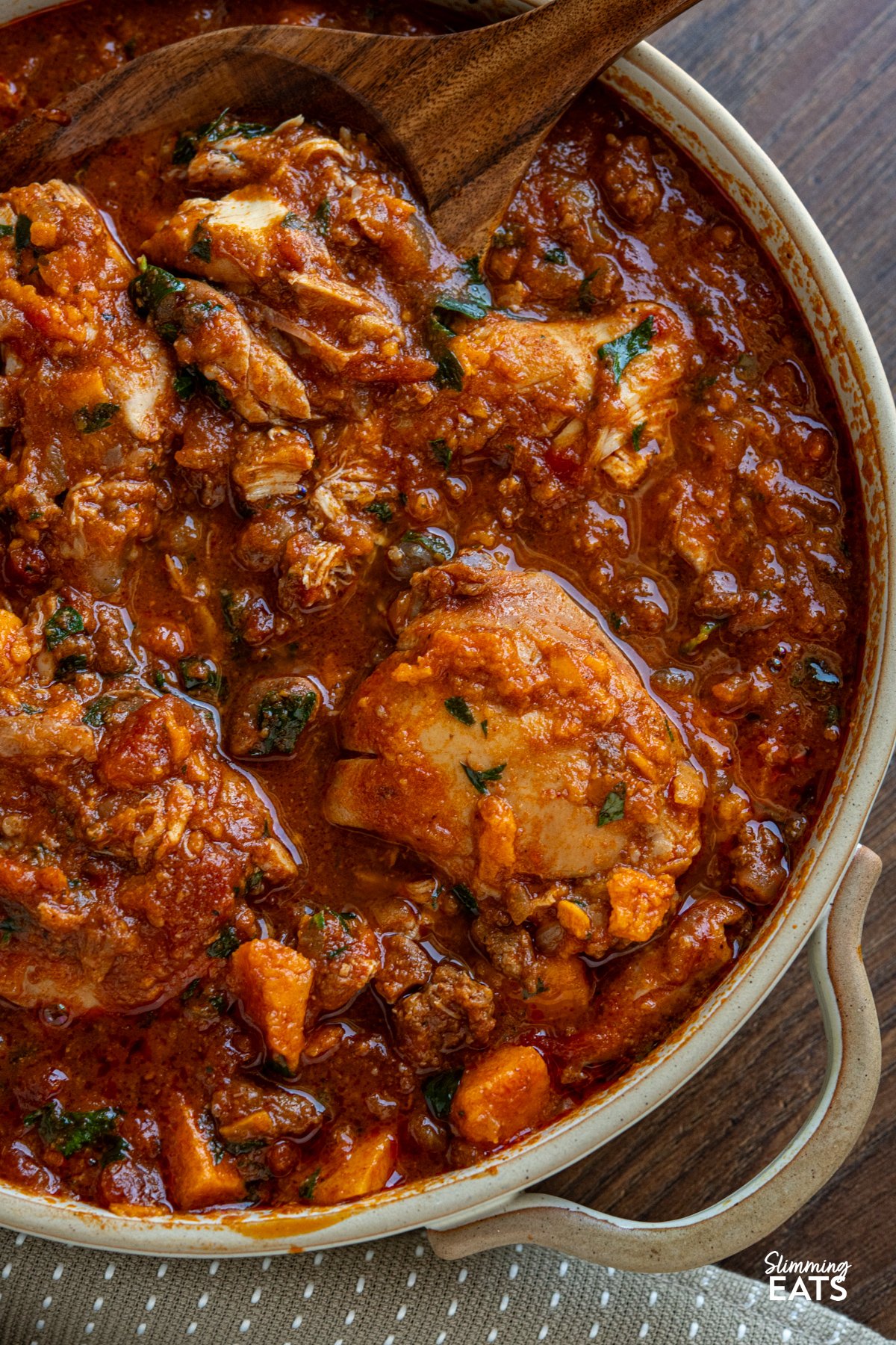 This Slow Cooker Chicken, Chorizo and Sweet Potato Stew is a hearty, flavour-packed meal that brings comfort and richness to any table. close up of Slow Cooker Chicken Chorizo Sweet Potato Stew in double handed beige ceramic dish