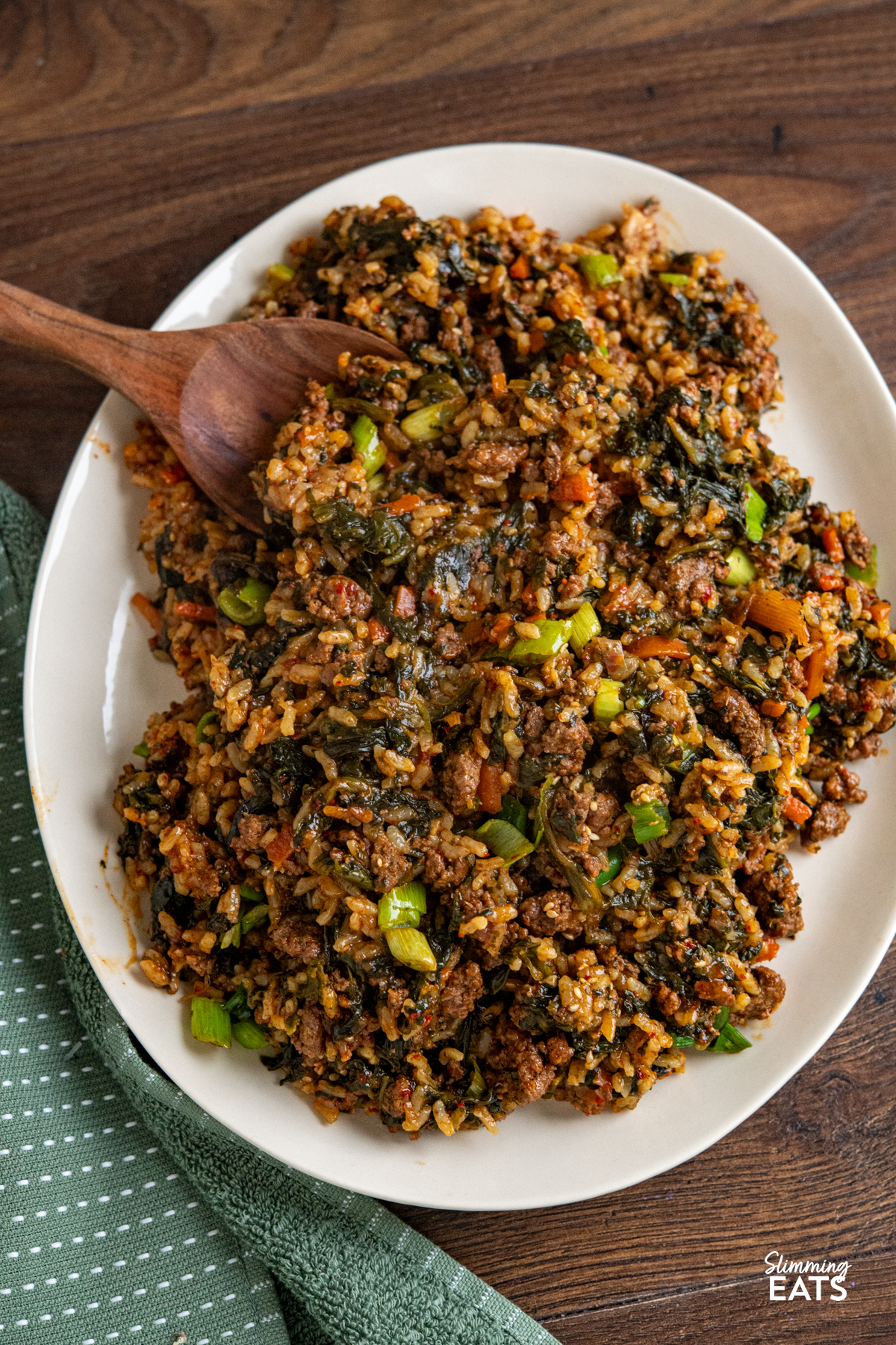 Enjoy the rich, savoury comfort of this Slow Cooker Korean Beef with Spinach and Rice. Ground beef simmers with garlic, ginger, and a sauce where gochujang is the star, alongside spinach and rice for a complete, flavour packed meal. cooked Slow Cooker Korean Beef Spinach Rice on light beige oval plate with wooden spatula placed in rice.