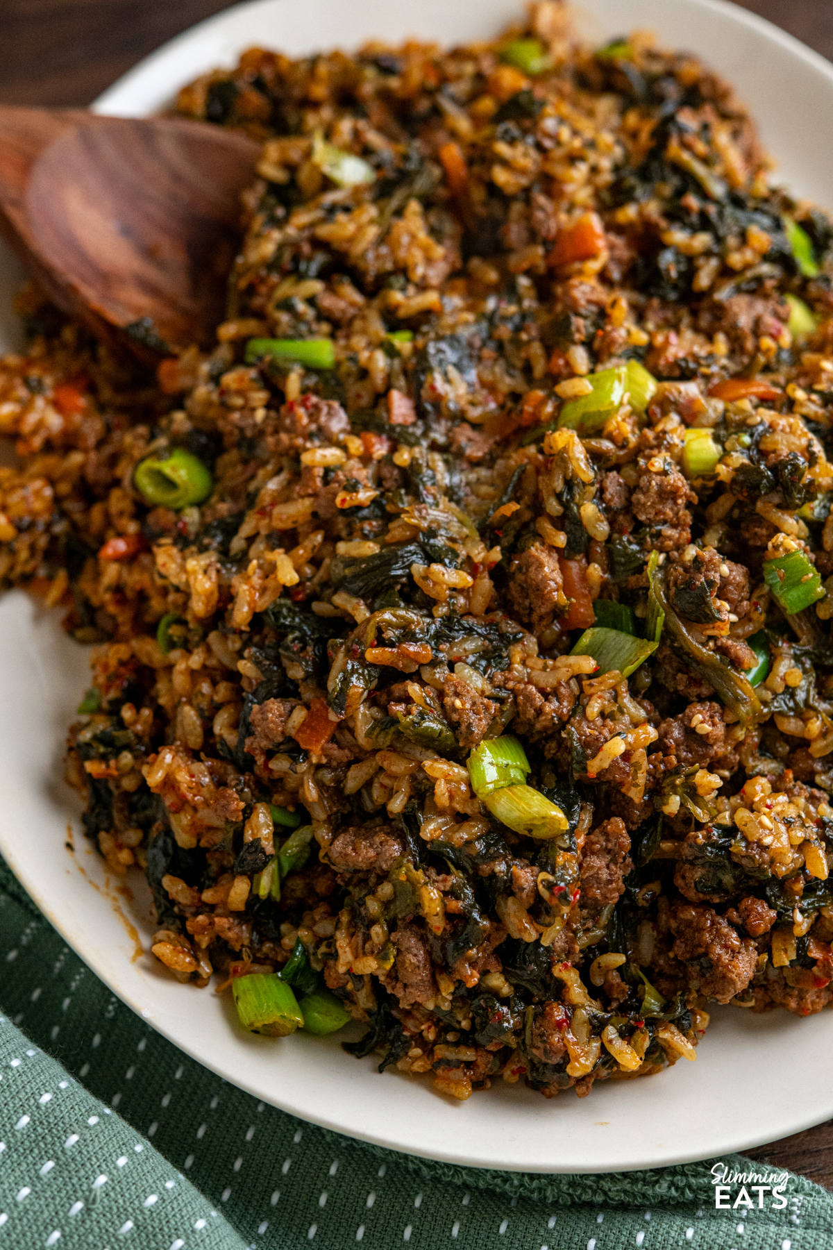 Enjoy the rich, savoury comfort of this Slow Cooker Korean Beef with Spinach and Rice. Ground beef simmers with garlic, ginger, and a sauce where gochujang is the star, alongside spinach and rice for a complete, flavour packed meal. close up of Slow Cooker Korean Beef Spinach Rice on light beige oval plate with wooden serving spatula place in rice