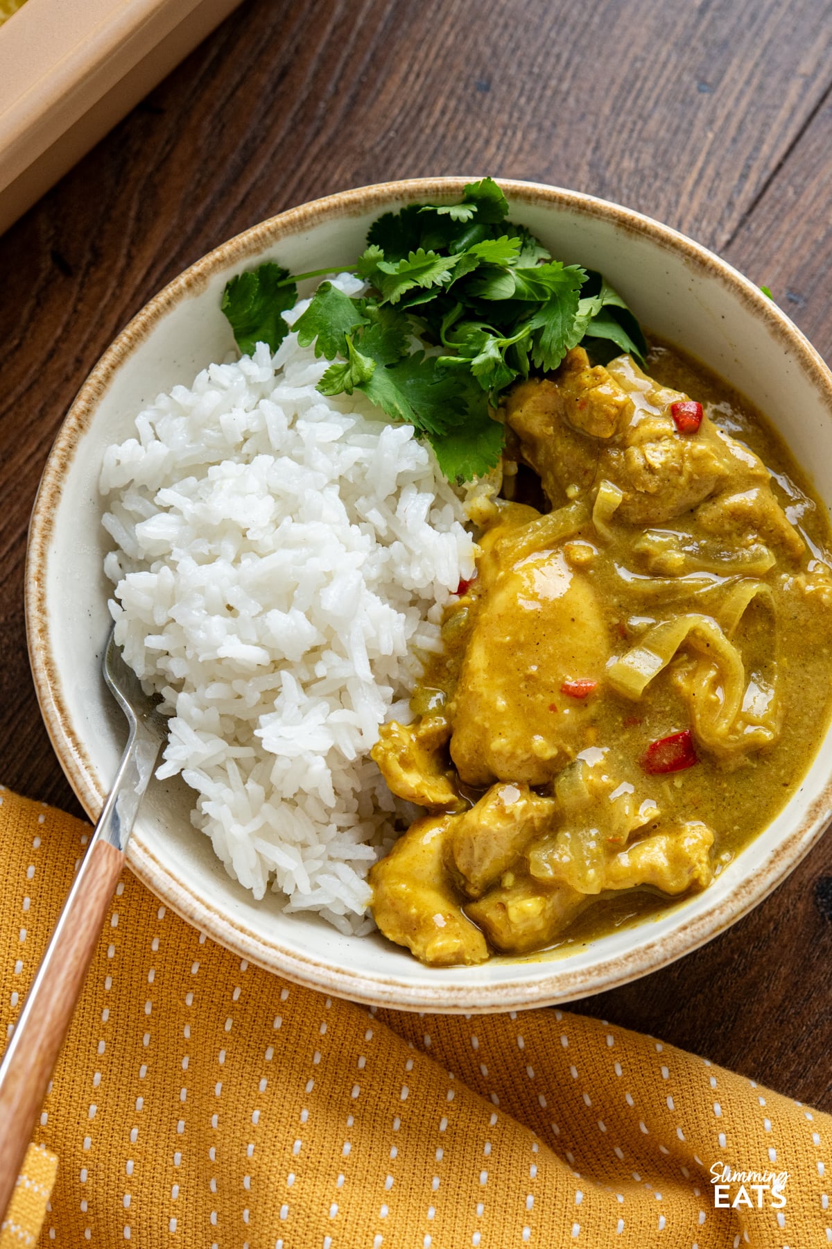 Enjoy a fuss-free, flavour-packed dinner with this Slow Cooker Coconut Sweet Chilli Chicken Curry, where tender chicken meets a creamy, mildly sweet sauce. close up of Slow Cooker Coconut Sweet Chilli Chicken Curry portion in white bowl with beige rim served with jasmine rice and some fresh coriander