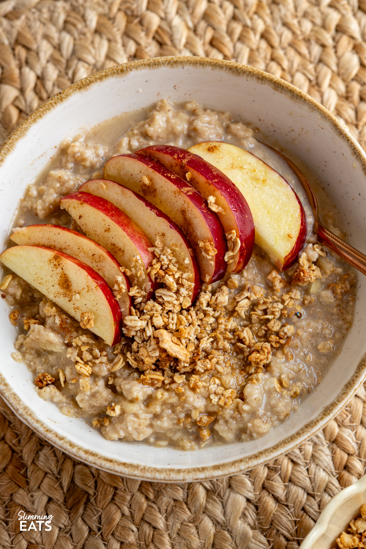 Start your day with this simple and comforting Apple Cinnamon Oatmeal bowl, packed with warming spices, crisp apple and low sugar granola topping. close up of Bowl of apple cinnamon oatmeal topped with low sugar granola