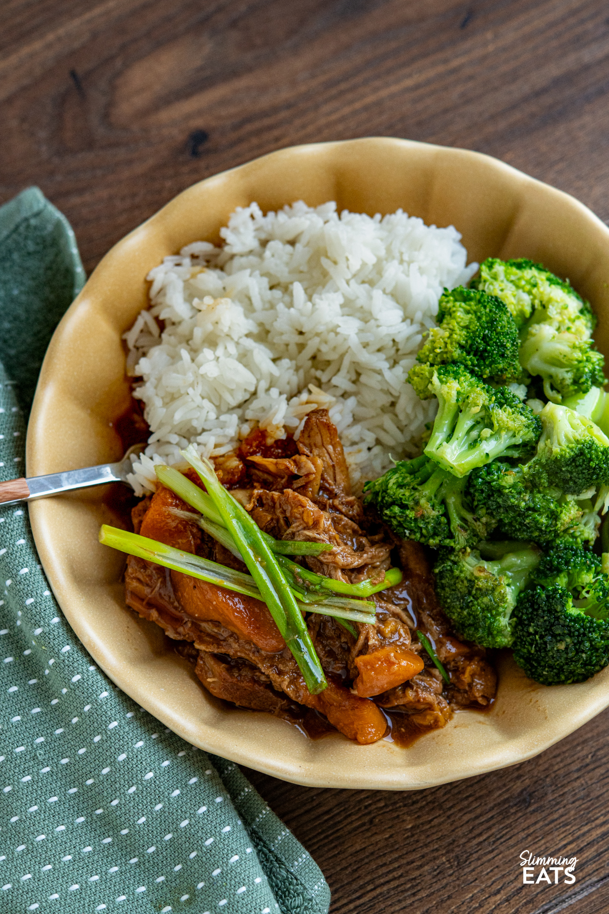 Slow cooker ginger peach pork is the definition of an easy, no fuss meal. You toss a few ingredients into the slow cooker, get on with your day and come back to a family dinner that is warm, comforting and wonderfully simple. cooked Slow Cooker Ginger Peach Pork in a yellow bowl served with rice and steamed broccoli