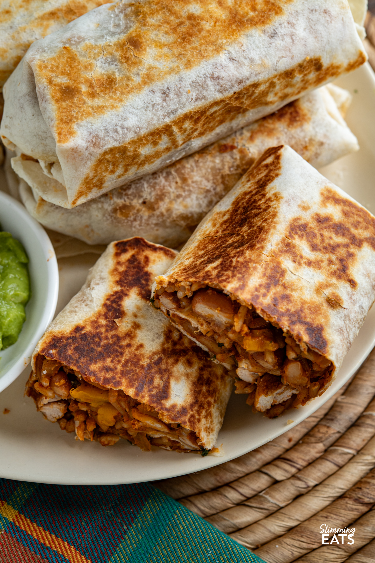 These one pan chicken rice burritos combine tender chicken, peppers, pinto beans and melted cheese for a quick, flavour-packed dinner. close up of One Pan Chicken Rice Burritos on a oval cream plate