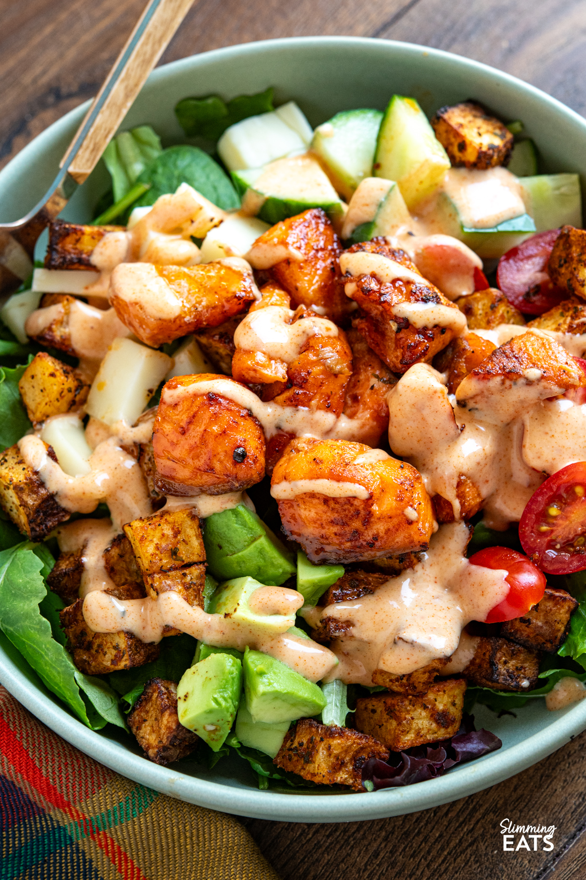 close up of Air Fryer Hot Honey Salmon Bowls  featuring salmon, potato, salad, avocado and gouda with dressing drizzle over the top