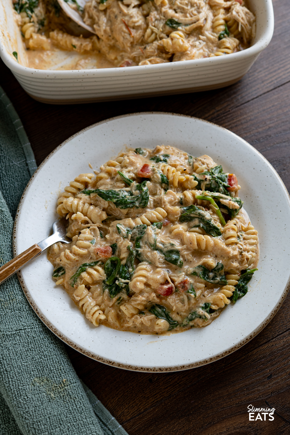 This Slow Cooker Creamy Garlic Chicken Spinach Pasta is an effortless, all-in-one slow cooker meal that’s rich, comforting, and perfect for busy weeknights. serving of Slow Cooker Creamy Garlic Chicken Spinach Pasta on a white plate with fork placed on left.