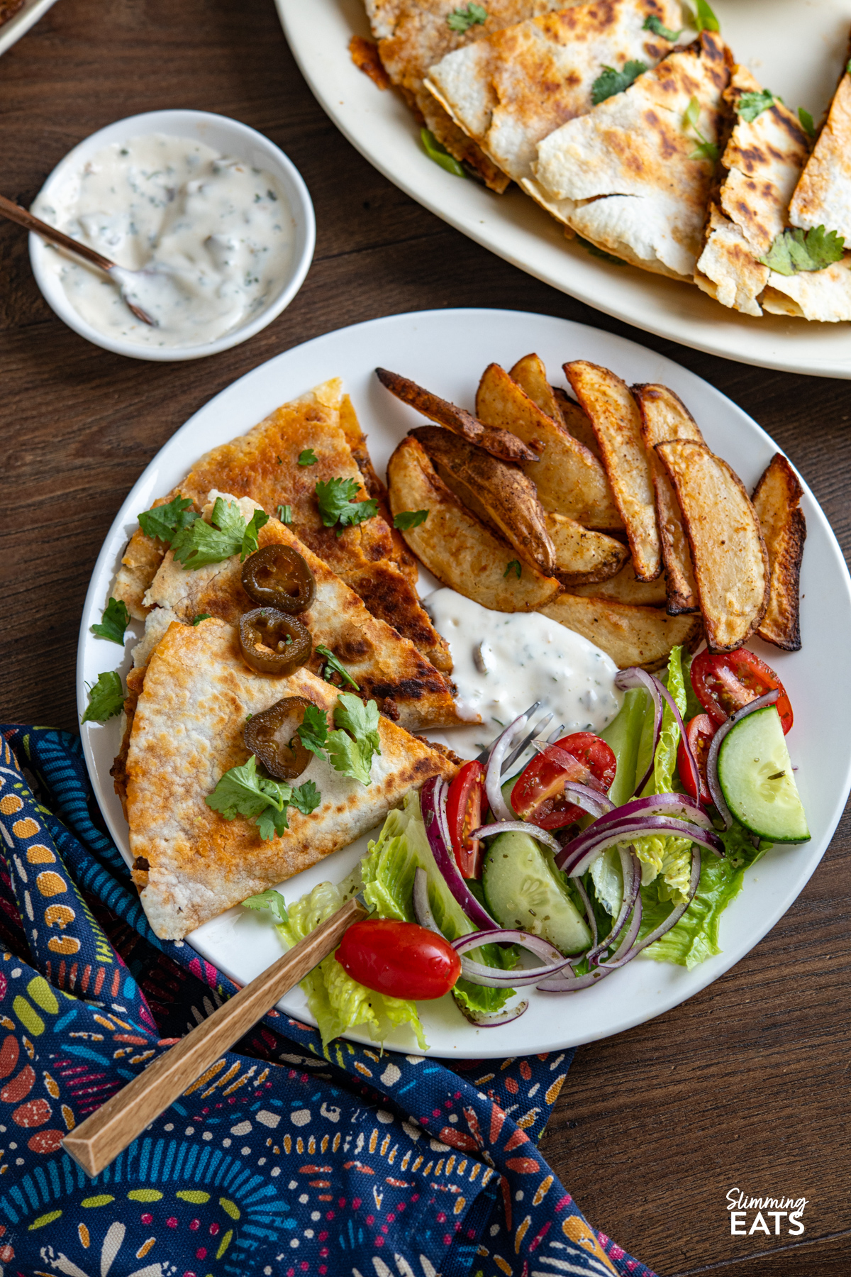 portion of Cheesy BBQ Beef Jalapeno Quesadillas triangles on a plate with potato wedges and mixed salad and some creamy dip and pickled jalapenos