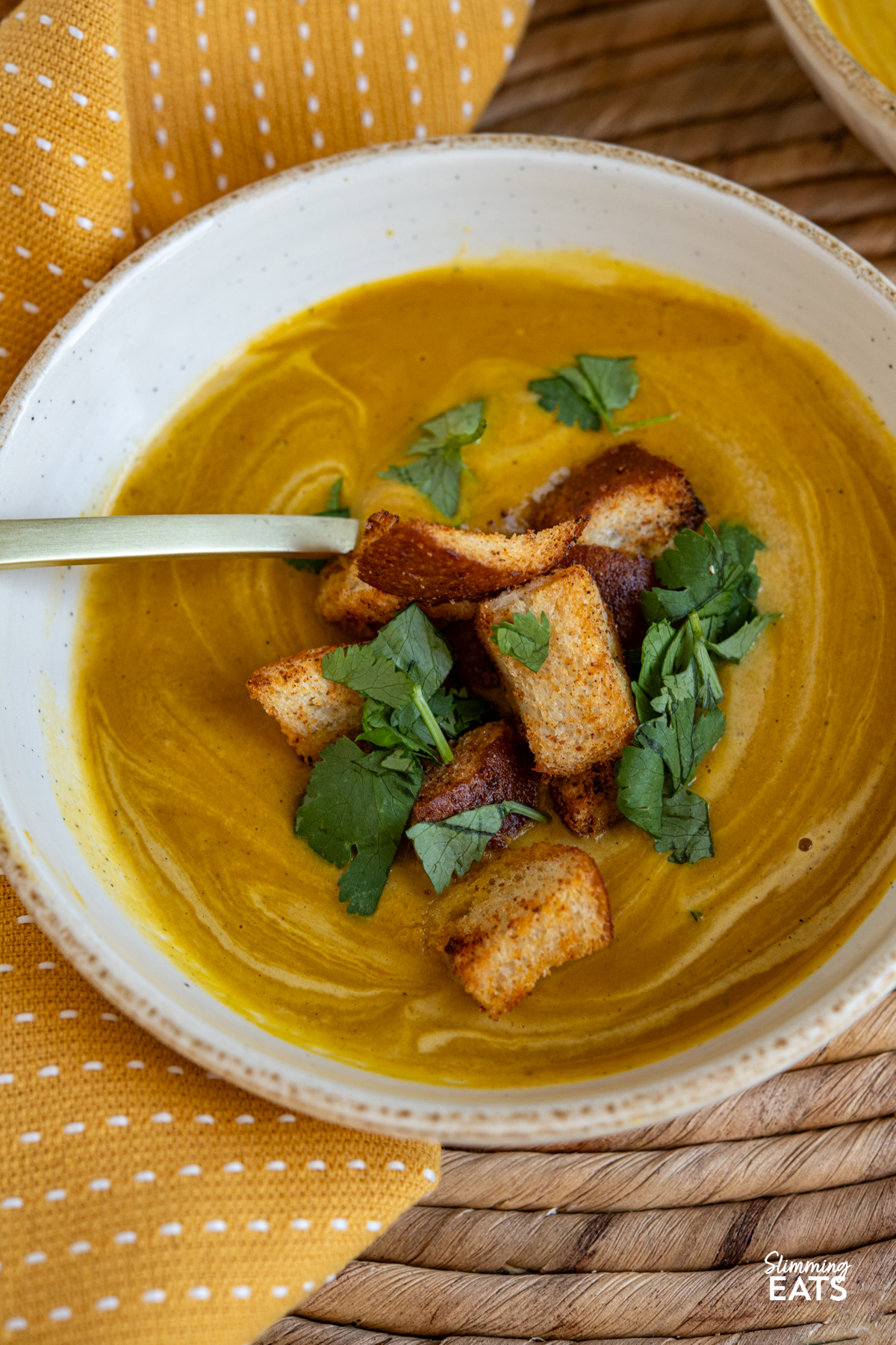 close up of white bowl with serving of Roasted Ras el Hanout Carrot Soup topped with homemade croutons, and cilantro