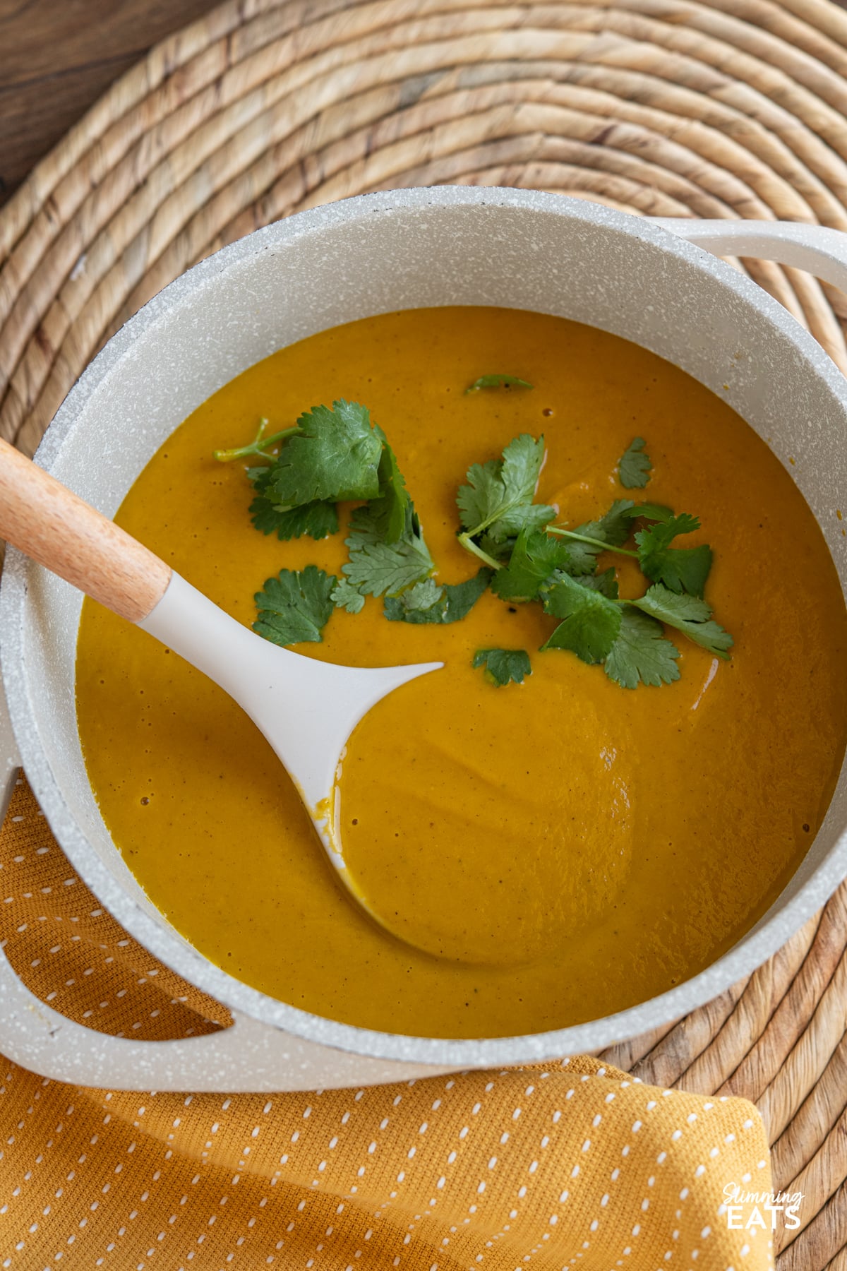 Roasted Ras el Hanout Carrot Soup in cream saucepan with ladle topped with coriander