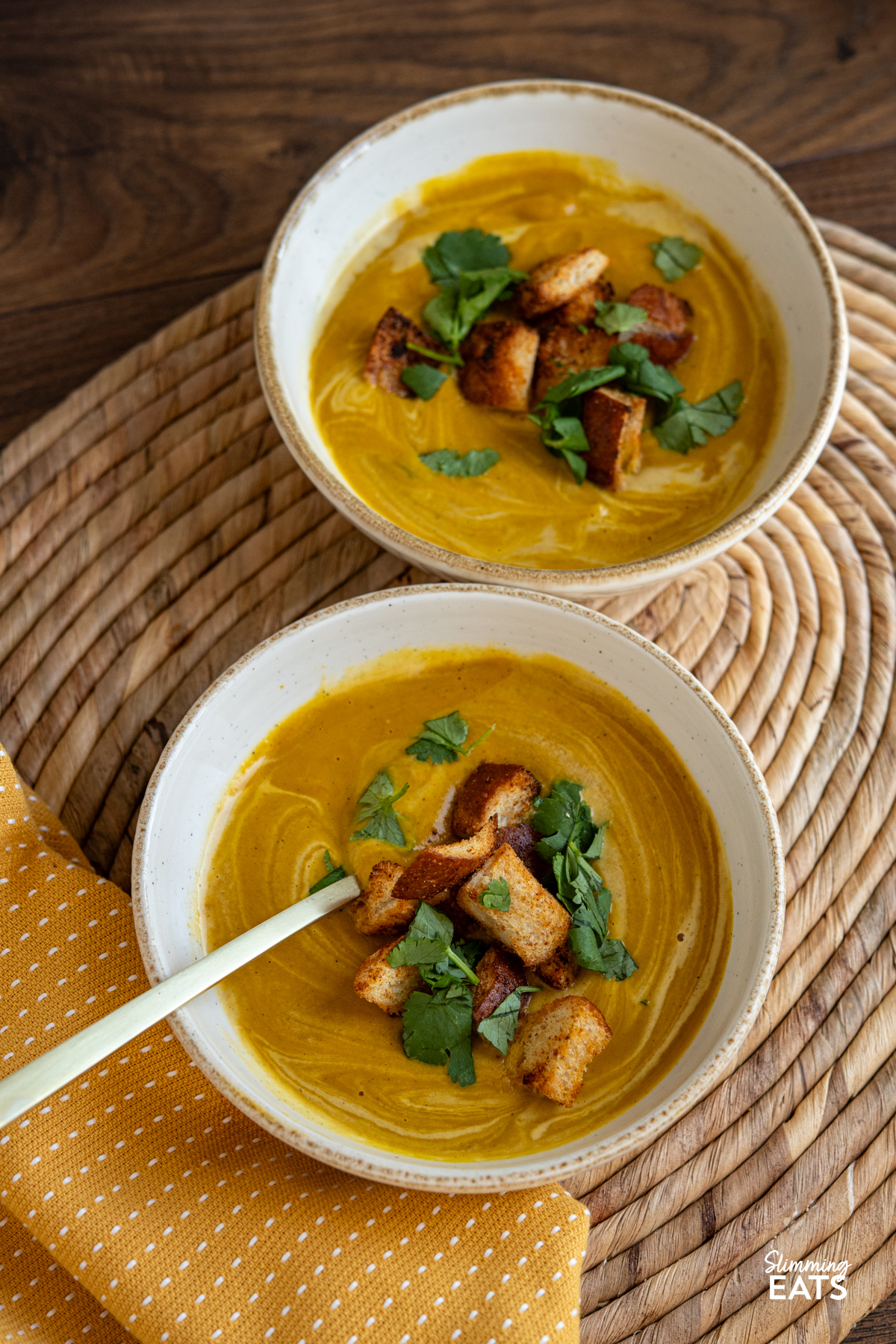 two white bowls with servings of Roasted Ras el Hanout Carrot Soup topped with homemade croutons and cilantro