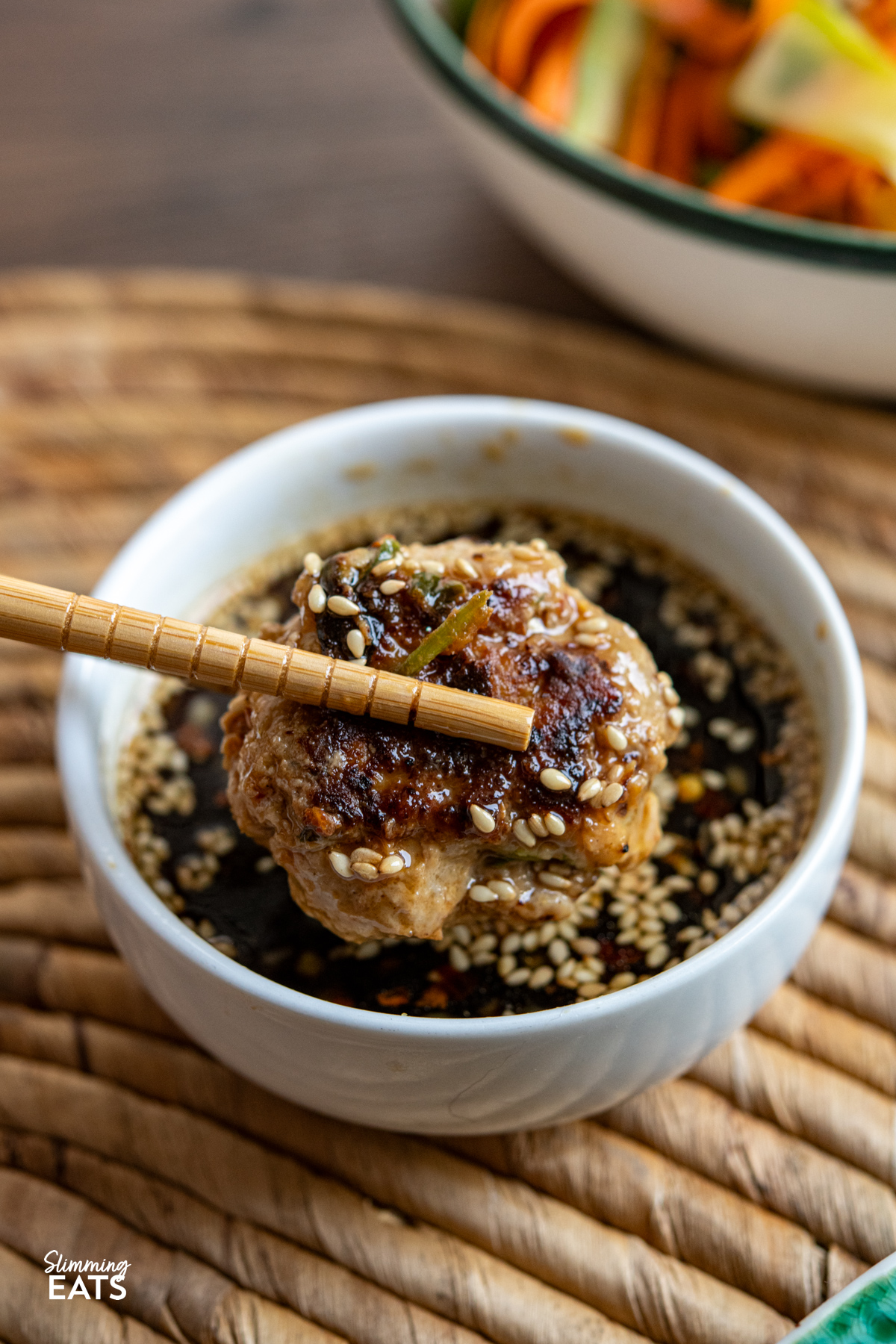 These juicy Asian Chicken Patties are packed with savoury flavour and served with a simple dipping sauce and fresh crunchy salad for an easy, delicious meal. asian chicken pattie being dipping into dipping sauce with chopsticks