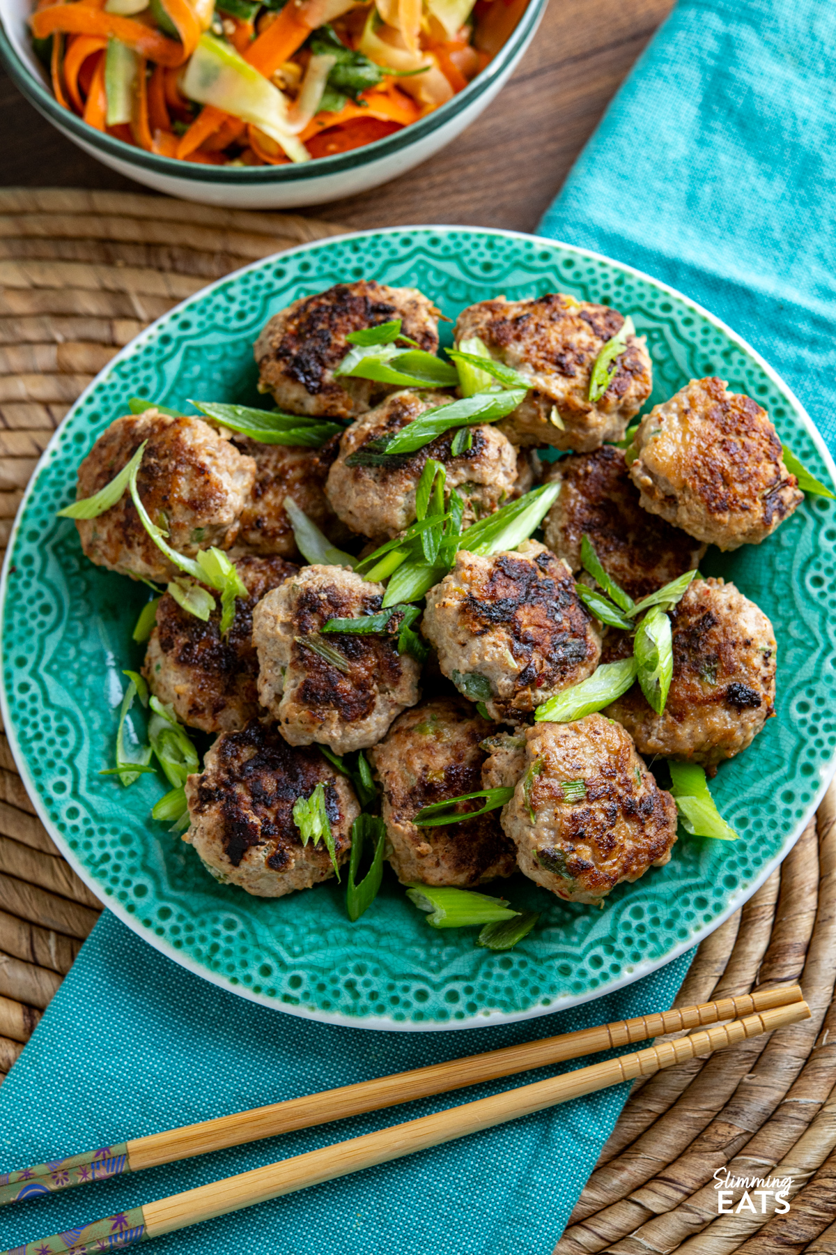 These juicy Asian Chicken Patties are packed with savoury flavour and served with a simple dipping sauce and fresh crunchy salad for an easy, delicious meal. close up of Asian Chicken Patties on jade coloured plate next to white bowl with green rim filled with cucumber and carrot salad