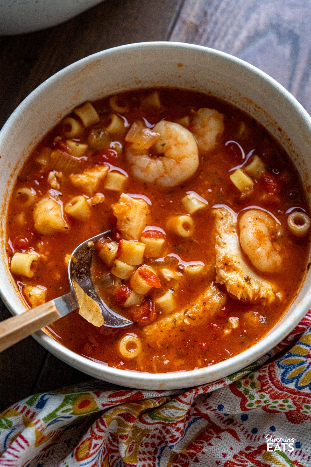 A rich and hearty Mediterranean-inspired seafood pasta soup made with monkfish, shrimp and tender ditalini in a deeply flavourful tomato broth. close up of serving of Fish and Pasta Soup in a cream coloured bowl with spoon