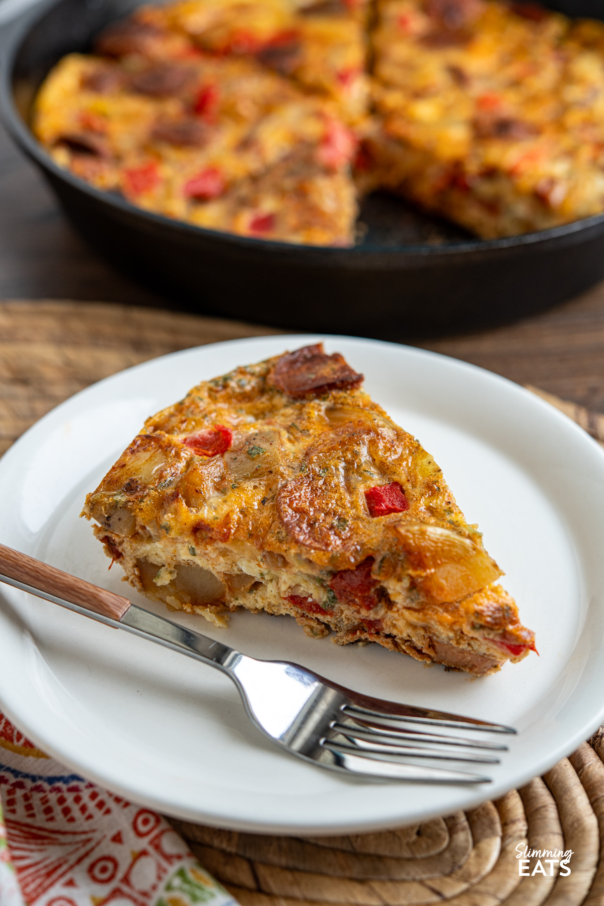 Spicy smoked sausage, tender potato, roasted red pepper and cheddar come together in this easy frittata that is perfect for brunch, lunch or a simple dinner. slice of Spicy Smoked Sausage and Potato Frittata on white plate with a fork