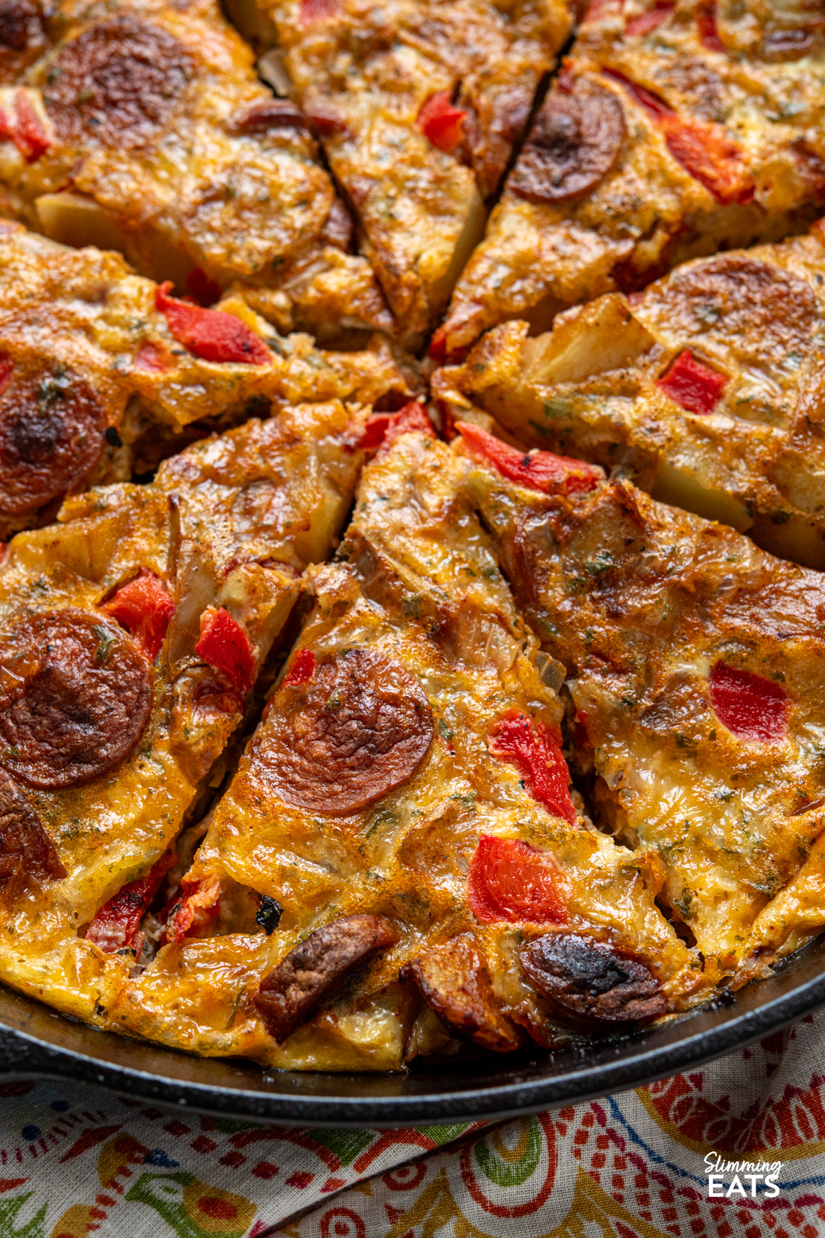 Spicy smoked sausage, tender potato, roasted red pepper and cheddar come together in this easy frittata that is perfect for brunch, lunch or a simple dinner. close up of Spicy Smoked Sausage and Potato Frittata sliced in a black cast iron skillet