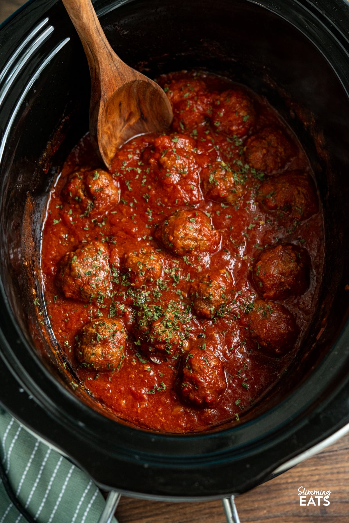 Slow Cooker Pesto Beef Meatballs are a comforting, flavour packed dinner with tender beef meatballs cooked in a rich tomato sauce. Pesto Beef Meatballs in tomato sauce in slow cooker with wooden spoon