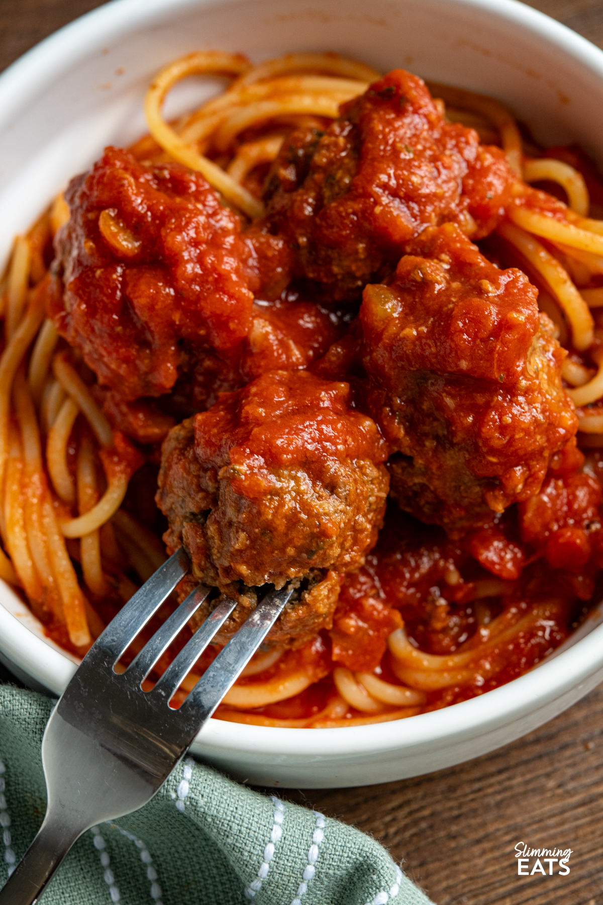 Slow Cooker Pesto Beef Meatballs are a comforting, flavour packed dinner with tender beef meatballs cooked in a rich tomato sauce. close up Slow Cooker Pesto Beef Meatballs mixed with spaghetti in a white bowl with fork