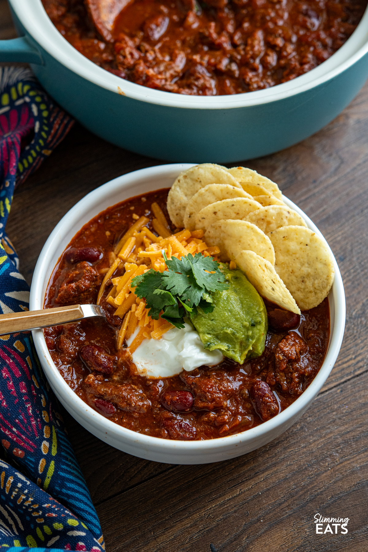 A hearty, flavour-packed slow cooker beef chilli with a rich salsa-infused sauce, tender beans and smoky spices for an easy meal the whole family will love. serving of Slow Cooker Salsa Beef Chilli in bowl with guacamole, soured cream, cheddar, cilantro and tortilla chips