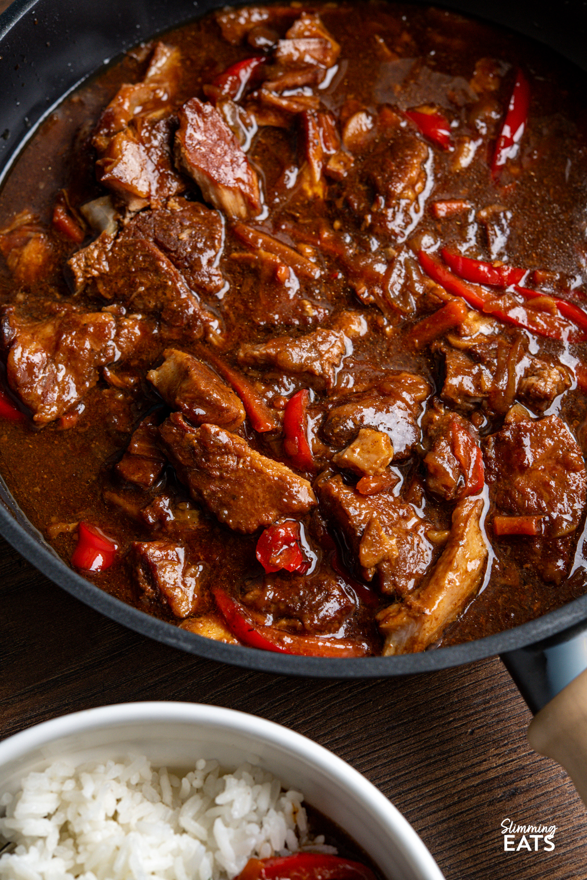 close up of Slow Cooker Honey Tamarind Pork in a skillet with bowl of rice visible off side