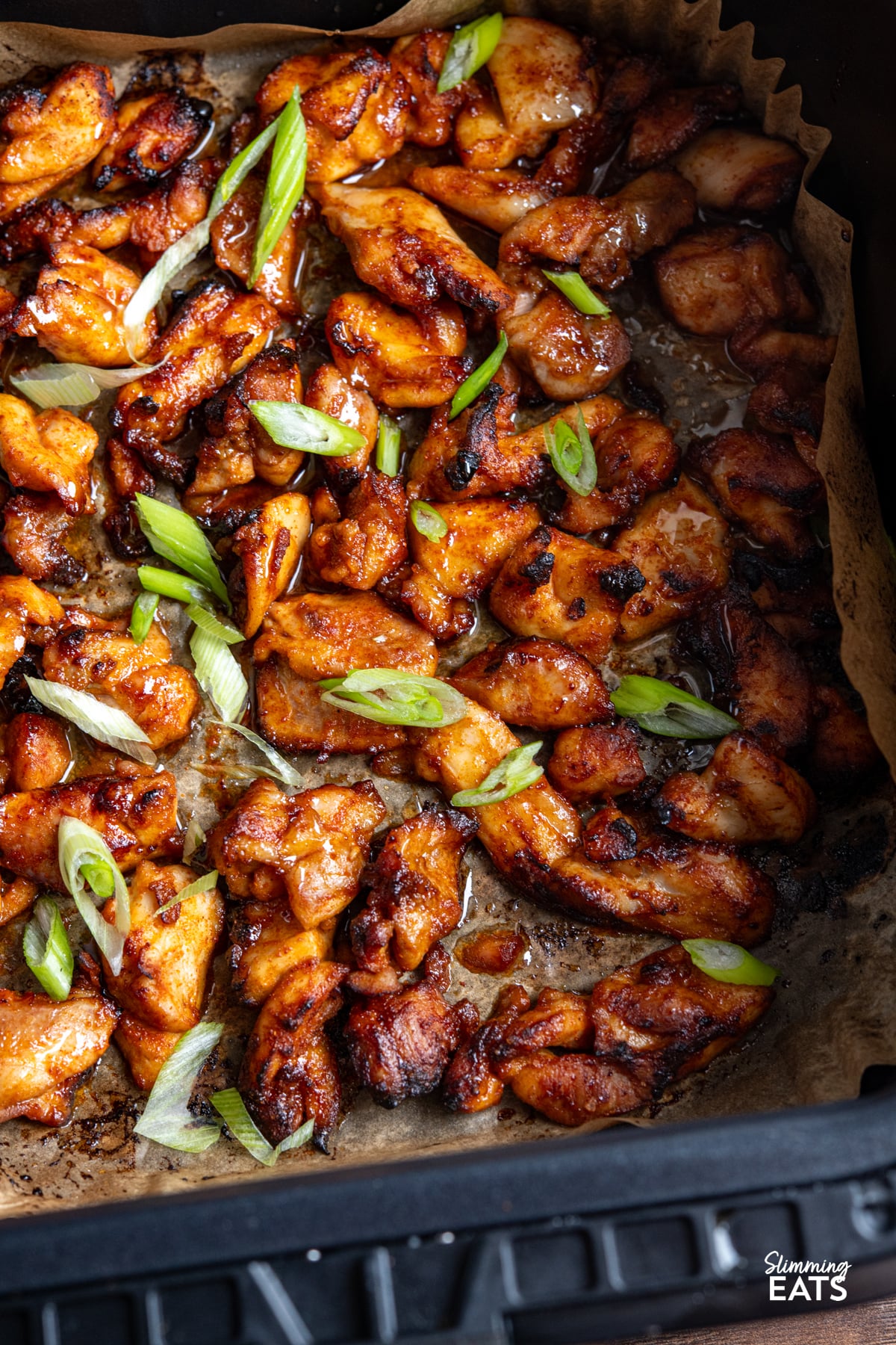 close up of Air Fryer Hot Honey Chicken on parchment sheet in air fryer basket sprinkled with green onion