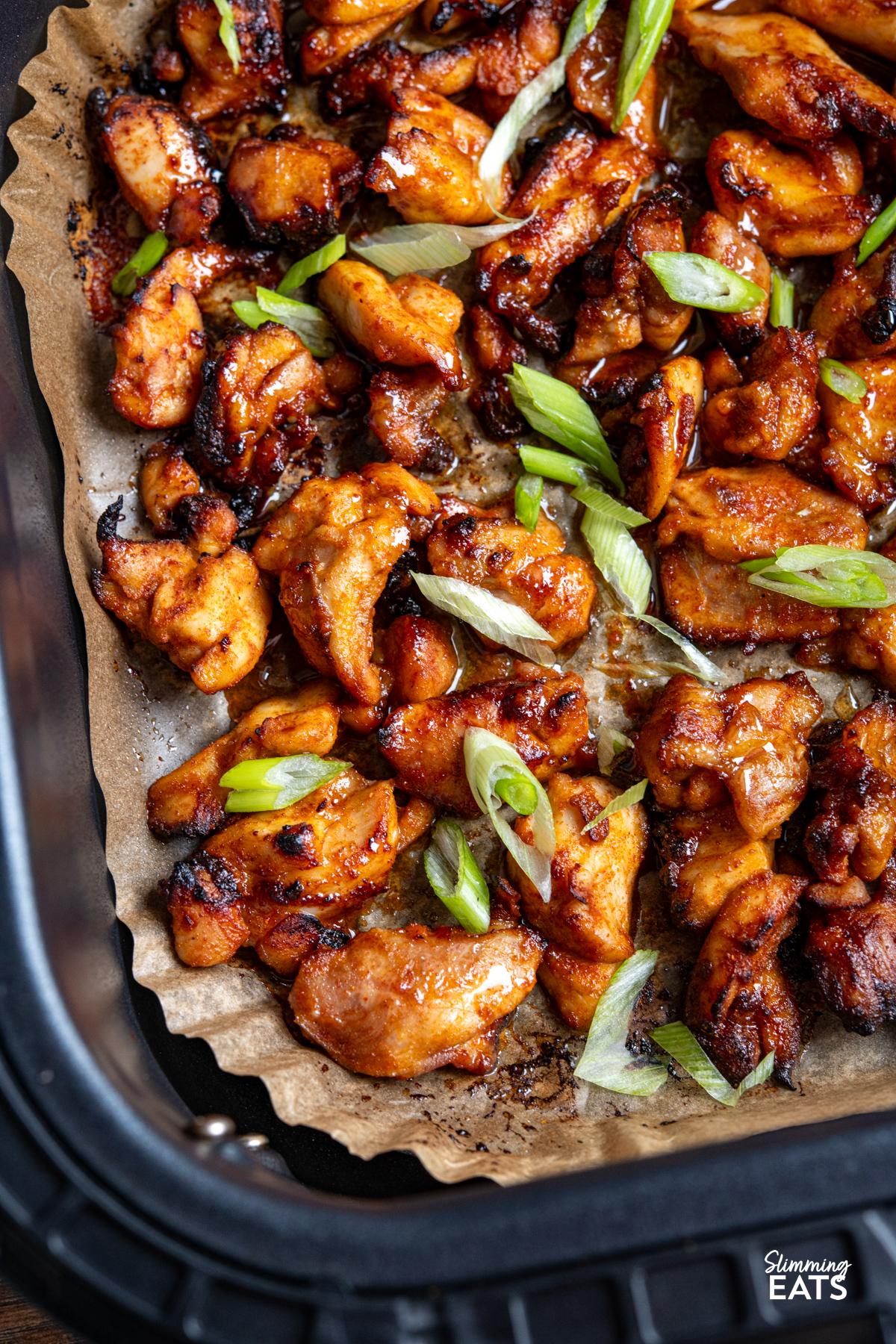 close up of Air Fryer Hot Honey Chicken on parchment sheet in air fryer basket sprinkled with green onion