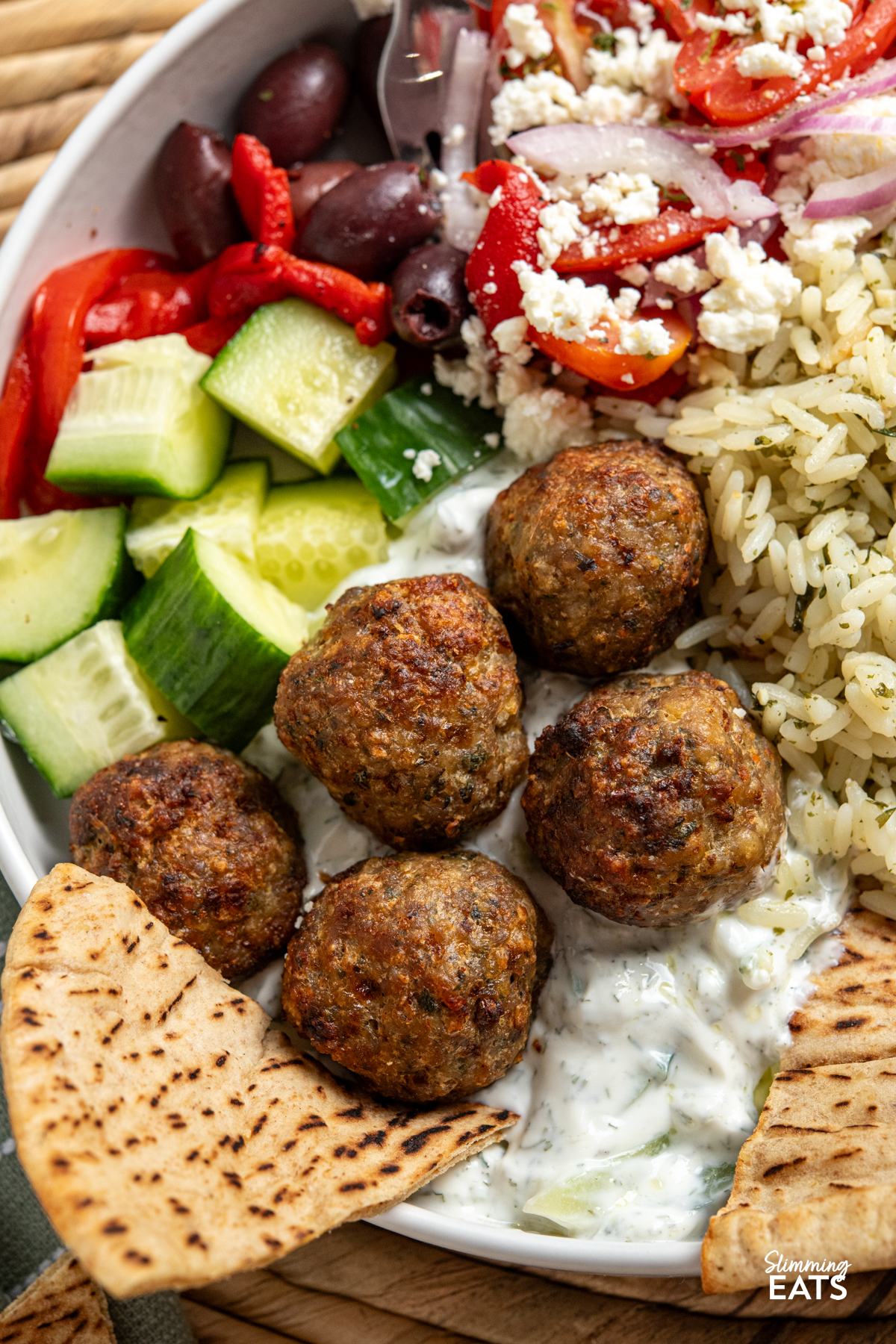 close up of Greek Turkey Meatball Bowls with herby rice, salad, tzatziki, feta, olives and warmed pitta bread