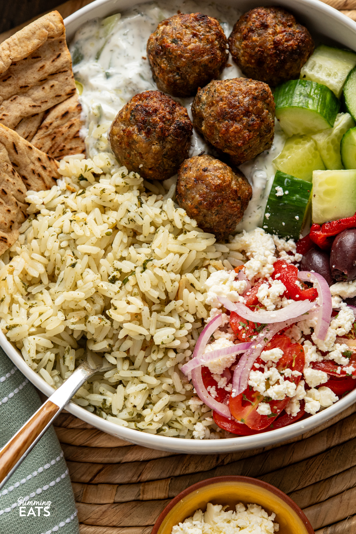 close up of Greek Turkey Meatball Bowls with herby rice, salad, tzatziki, feta, olives and warmed pitta bread