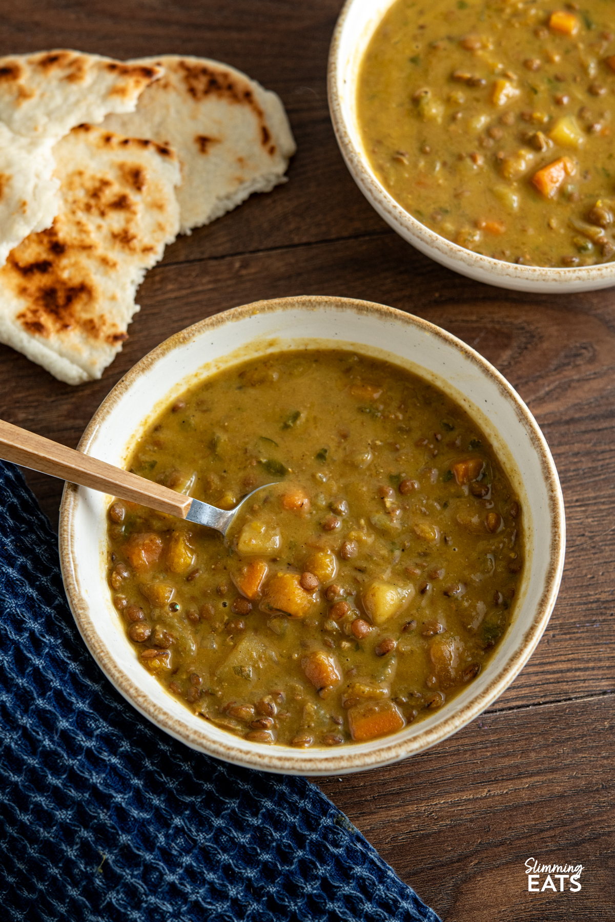 Slow Cooker Coconut Lentil Soup in a white bowl with beige rim, spoon placed in bowl with torn naan next to bowl