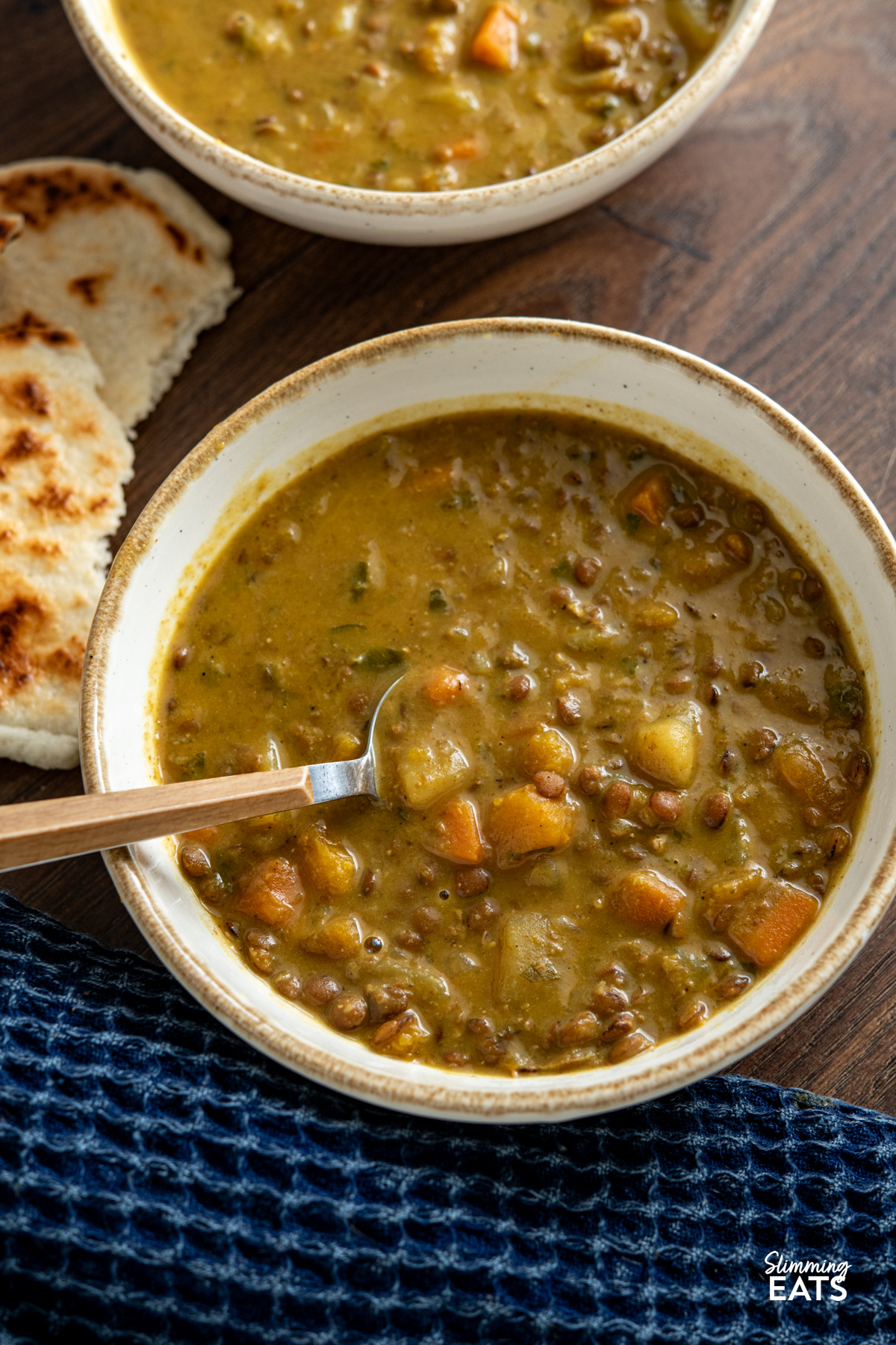 Slow Cooker Coconut Lentil Soup in a white bowl with beige rim, spoon placed in bowl with torn naan next to bowl