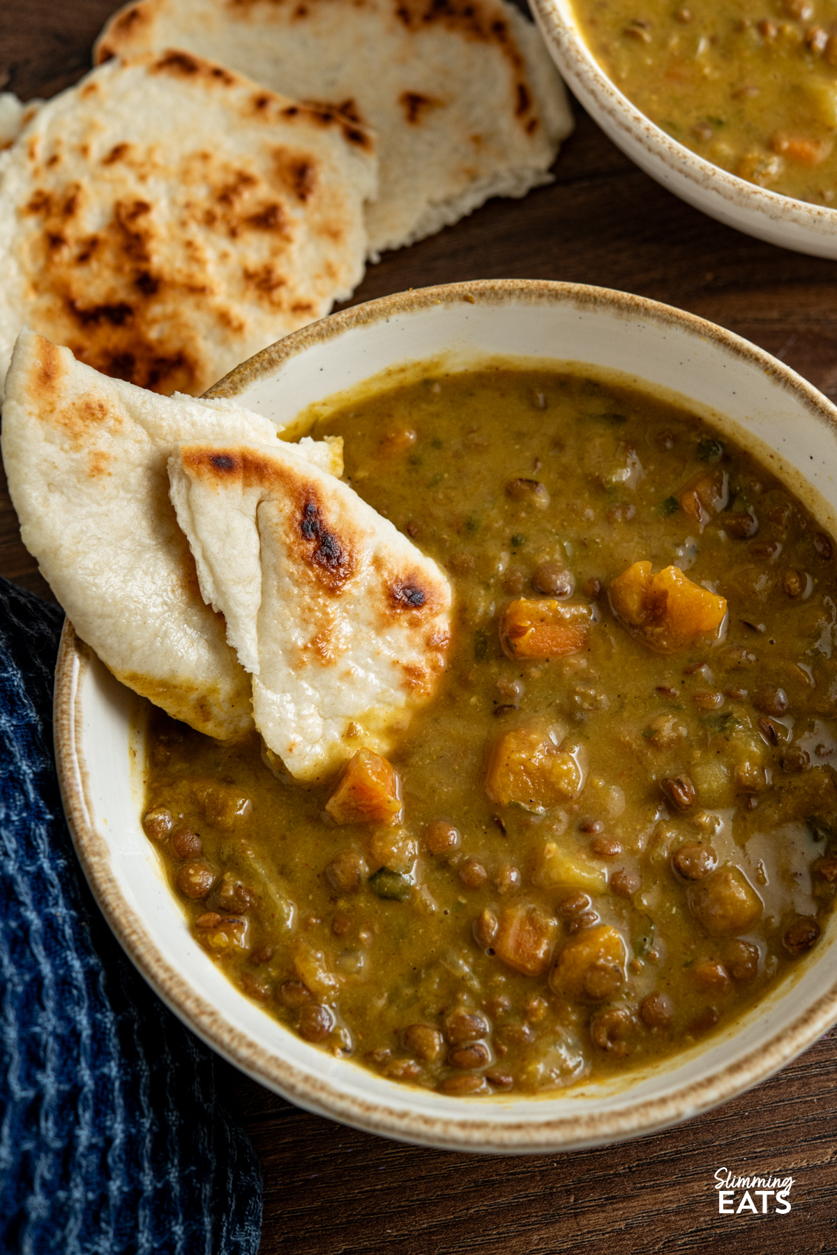 Slow Cooker Coconut Lentil Soup in a white bowl with a piece of torn naan bread dipped in soup 