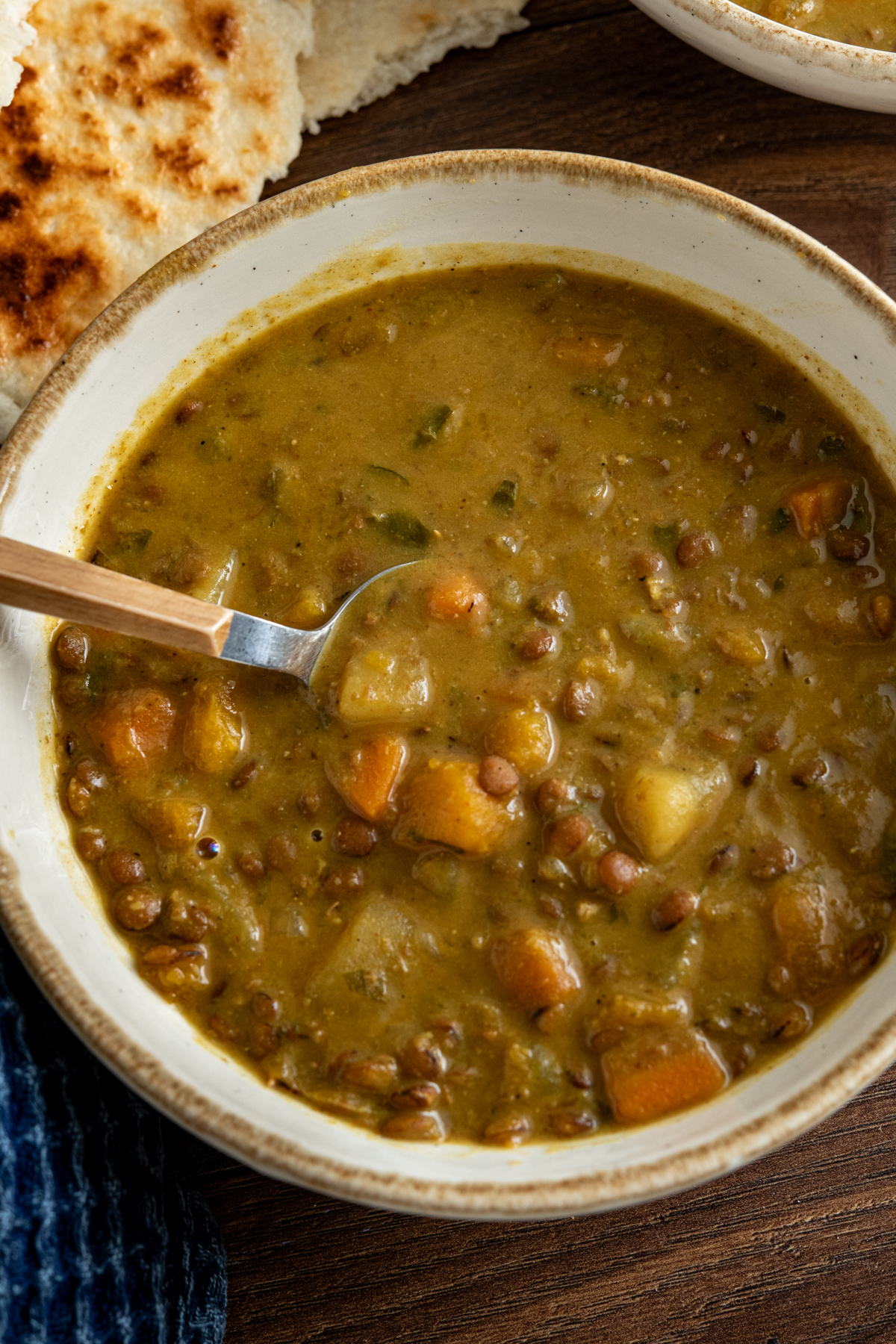 Slow Cooker Coconut Lentil Soup in a white bowl with beige rim, spoon placed in bowl with torn naan next to bowl