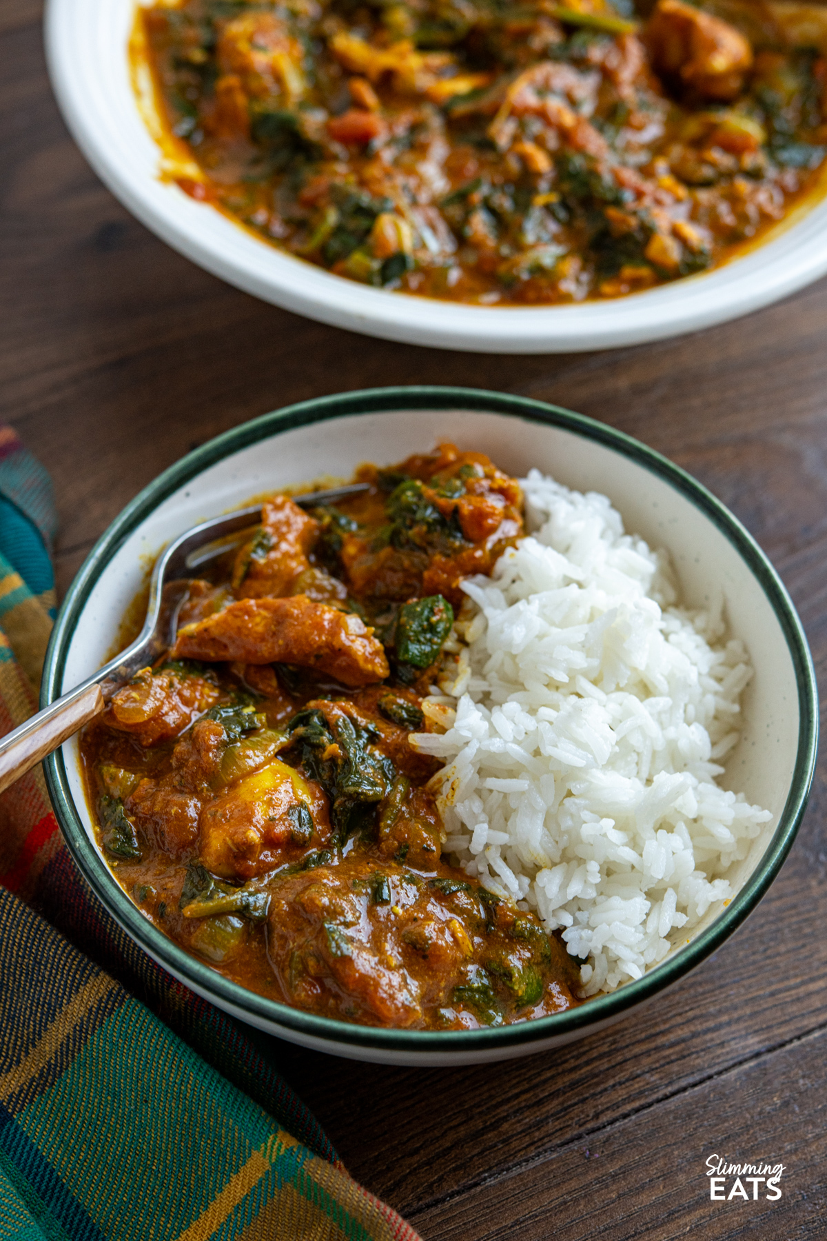 This slow cooker chicken spinach curry is an easy, delicious meal that is perfect for busy days. Tender chicken cooks away in a rich tomato curry sauce, with spinach stirred through at the end for a tasty family-friendly dish that is full of flavour. serving of Slow Cooker Easy Chicken Spinach Curry in a white bowl with a green rim