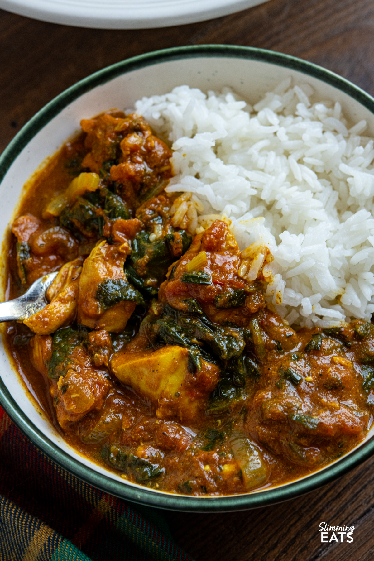 This slow cooker chicken spinach curry is an easy, delicious meal that is perfect for busy days. Tender chicken cooks away in a rich tomato curry sauce, with spinach stirred through at the end for a tasty family-friendly dish that is full of flavour. close up of serving of Slow Cooker Easy Chicken Spinach Curry in a white bowl with a green rim