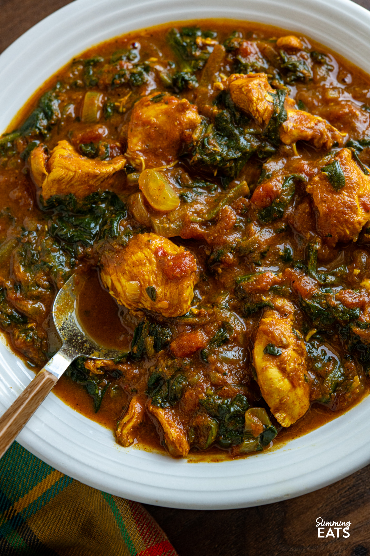This slow cooker chicken spinach curry is an easy, delicious meal that is perfect for busy days. Tender chicken cooks away in a rich tomato curry sauce, with spinach stirred through at the end for a tasty family-friendly dish that is full of flavour. close up of Slow Cooker Easy Chicken Spinach Curry in a white bowl