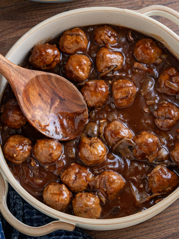 slow cooker salisbury meatballs in double handled casserole dish with wooden spoon