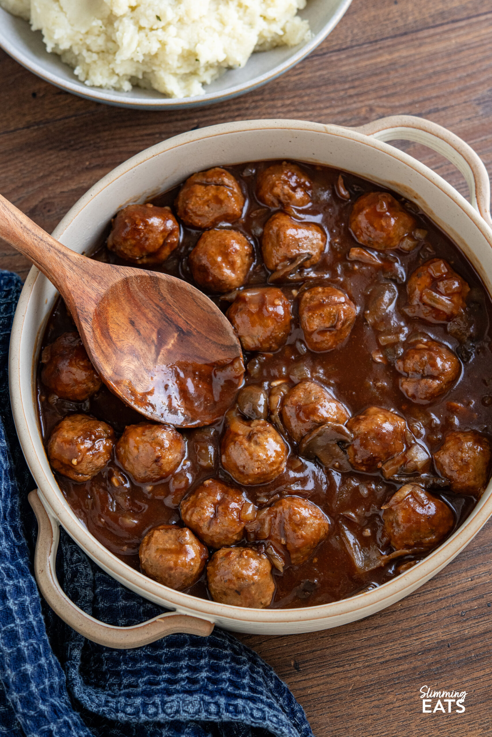 These slow cooker Salisbury meatballs are an easy, hearty dinner made with frozen meatballs simmered in a rich onion and mushroom gravy. Slow Cooker Salisbury Meatballs in a double handled casserole dish with wooden spoon