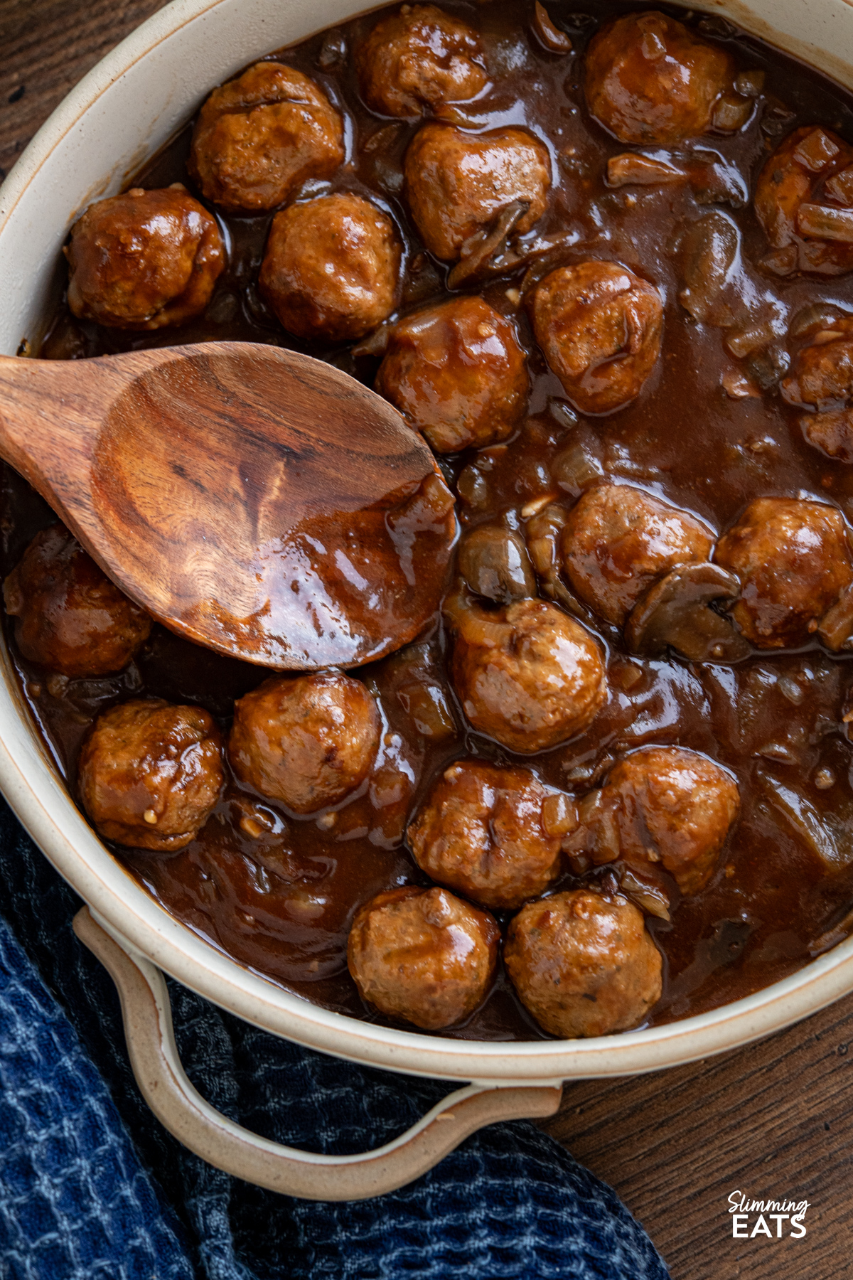 These slow cooker Salisbury meatballs are an easy, hearty dinner made with frozen meatballs simmered in a rich onion and mushroom gravy. close up of Slow Cooker Salisbury Meatballs in a double handled casserole dish with wooden spoon