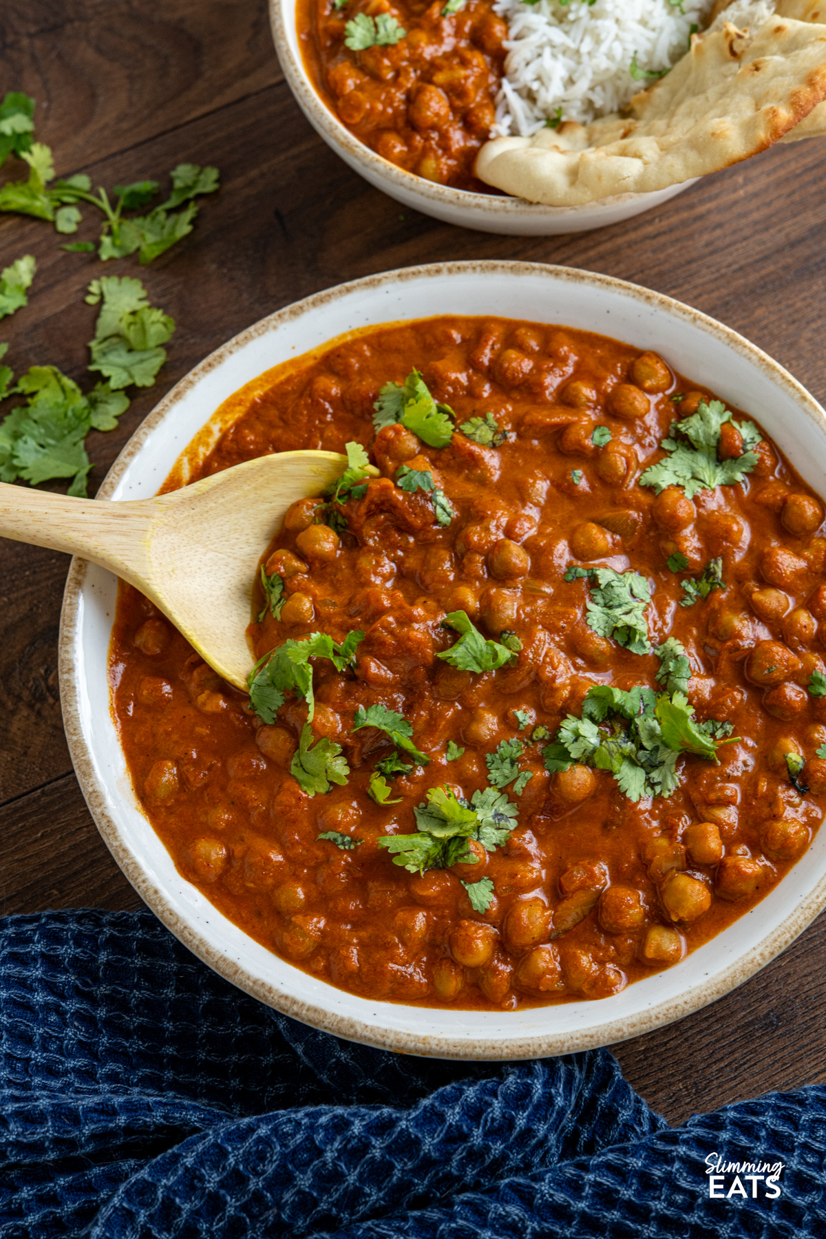 Slow Cooker Tomato Chickpea Curry in a large white bowl with beige rim, curry wooden spoon placed in bowl