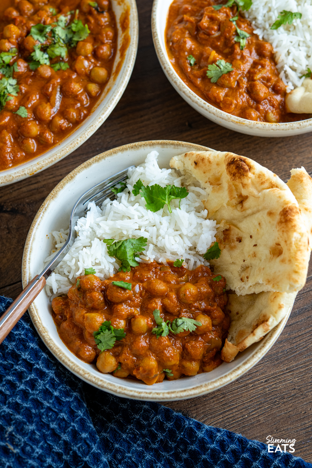 serving of  Slow Cooker Tomato Chickpea Curry in a white bowl with beige rim with white rice and torn naan, garnished with coriander