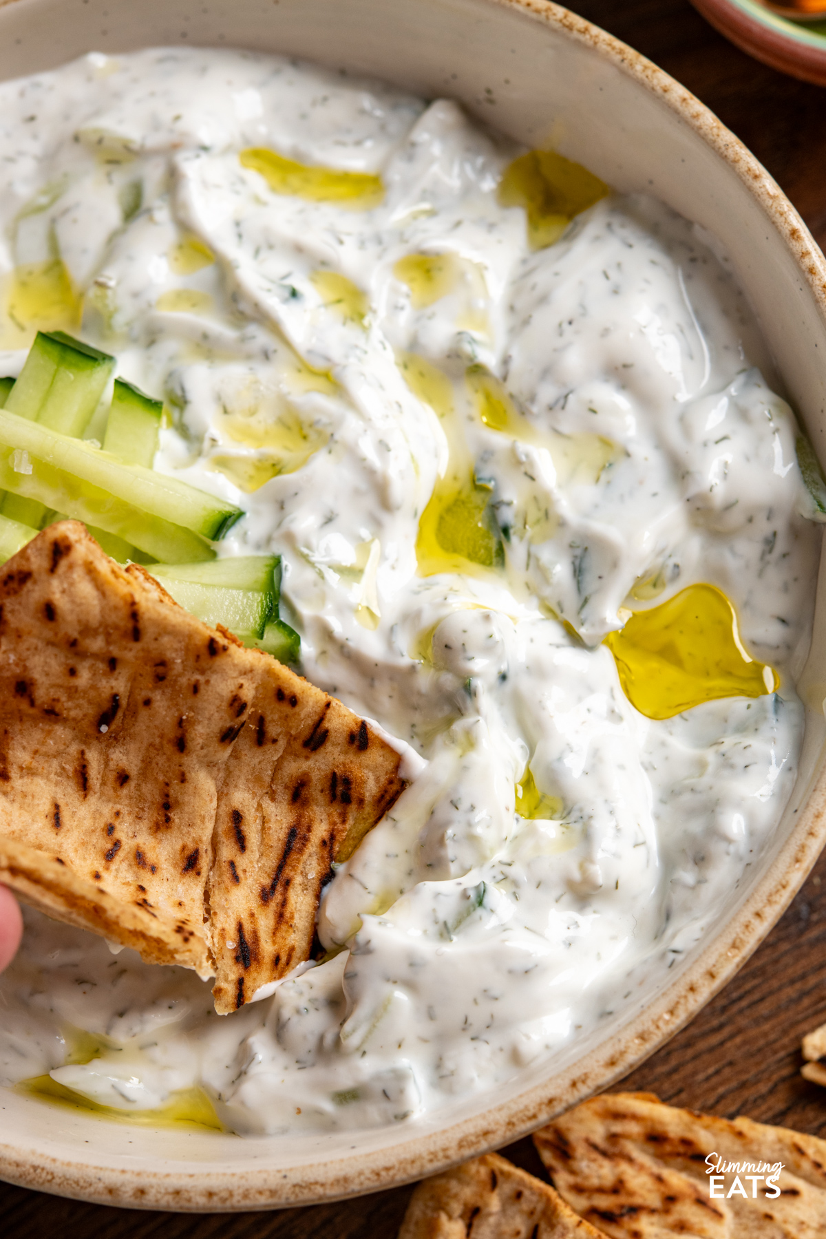 This easy tzatziki dip is cool, creamy and packed with fresh flavour, making it perfect for dipping, drizzling or serving alongside all your favourite Mediterranean-inspired dishes. close up of pita being dipped in tzatziki dip in a bowl