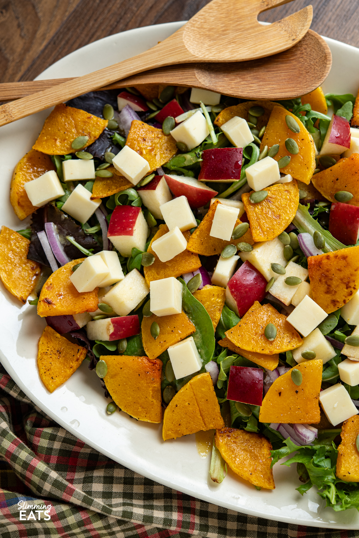 Butternut Squash Salad with Apple and Cheddar on oval cream plate with wooden salad spoons placed on left