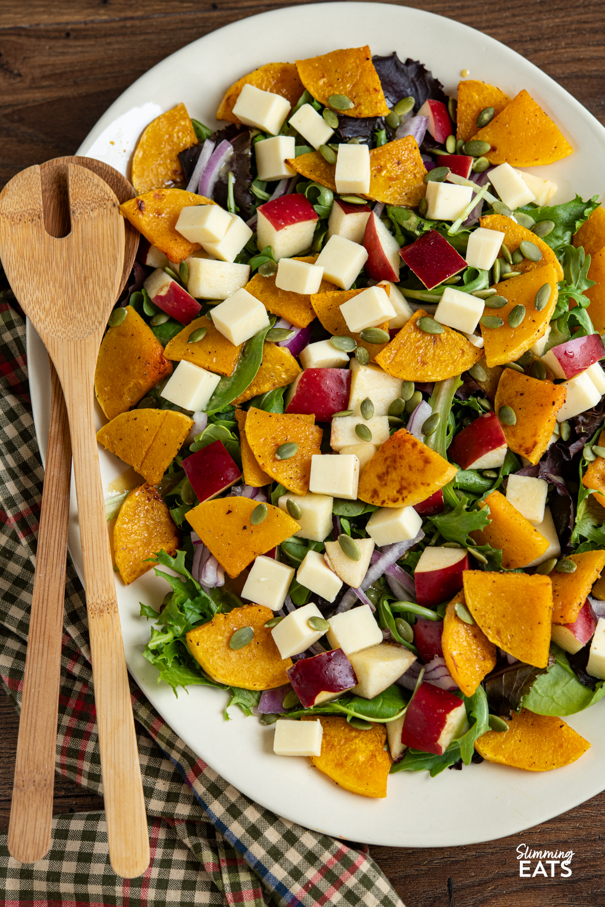 Butternut Squash Salad with Apple and Cheddar on oval cream plate with wooden salad spoons placed on left