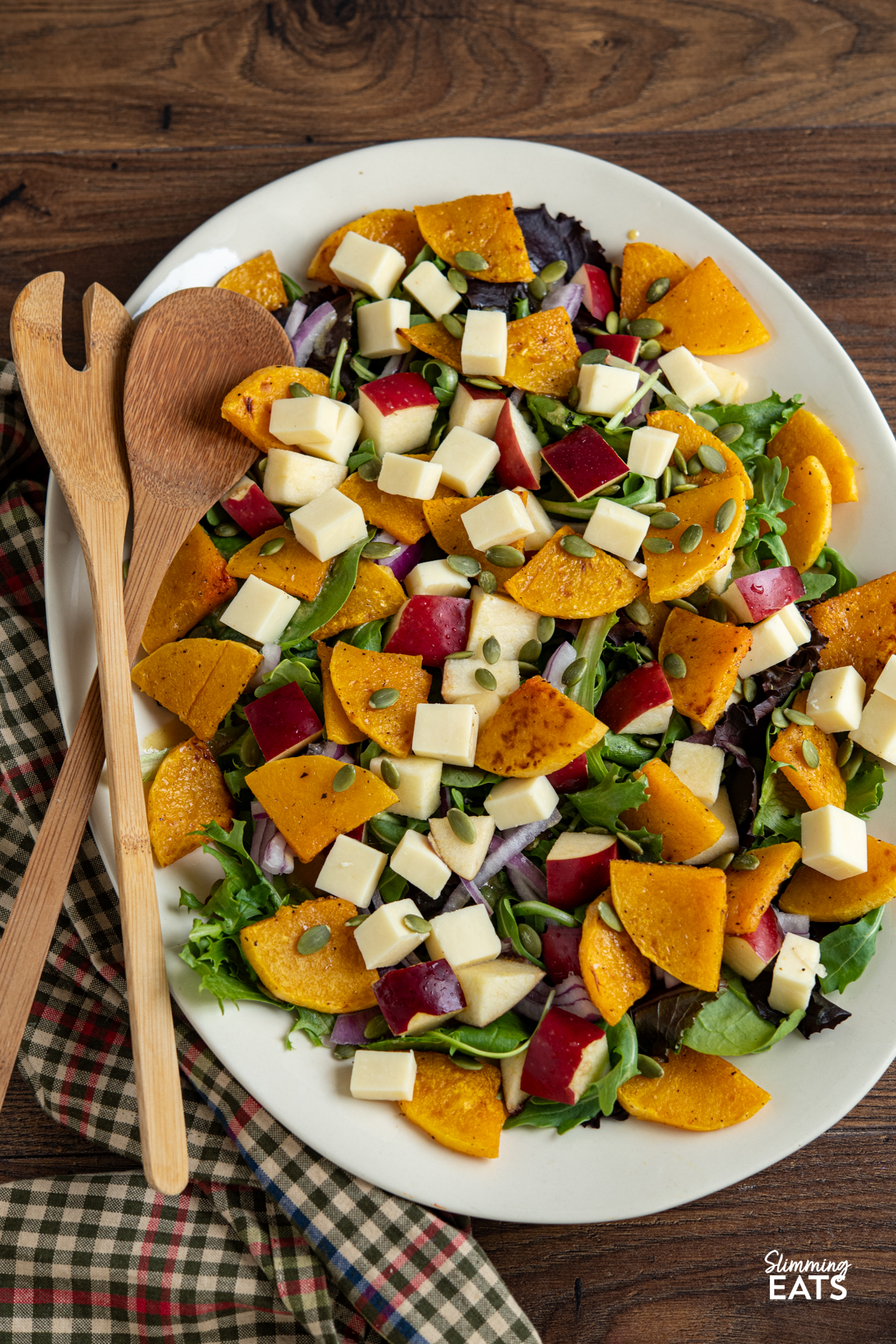Butternut Squash Salad with Apple and Cheddar on oval cream plate with wooden salad spoons placed on left