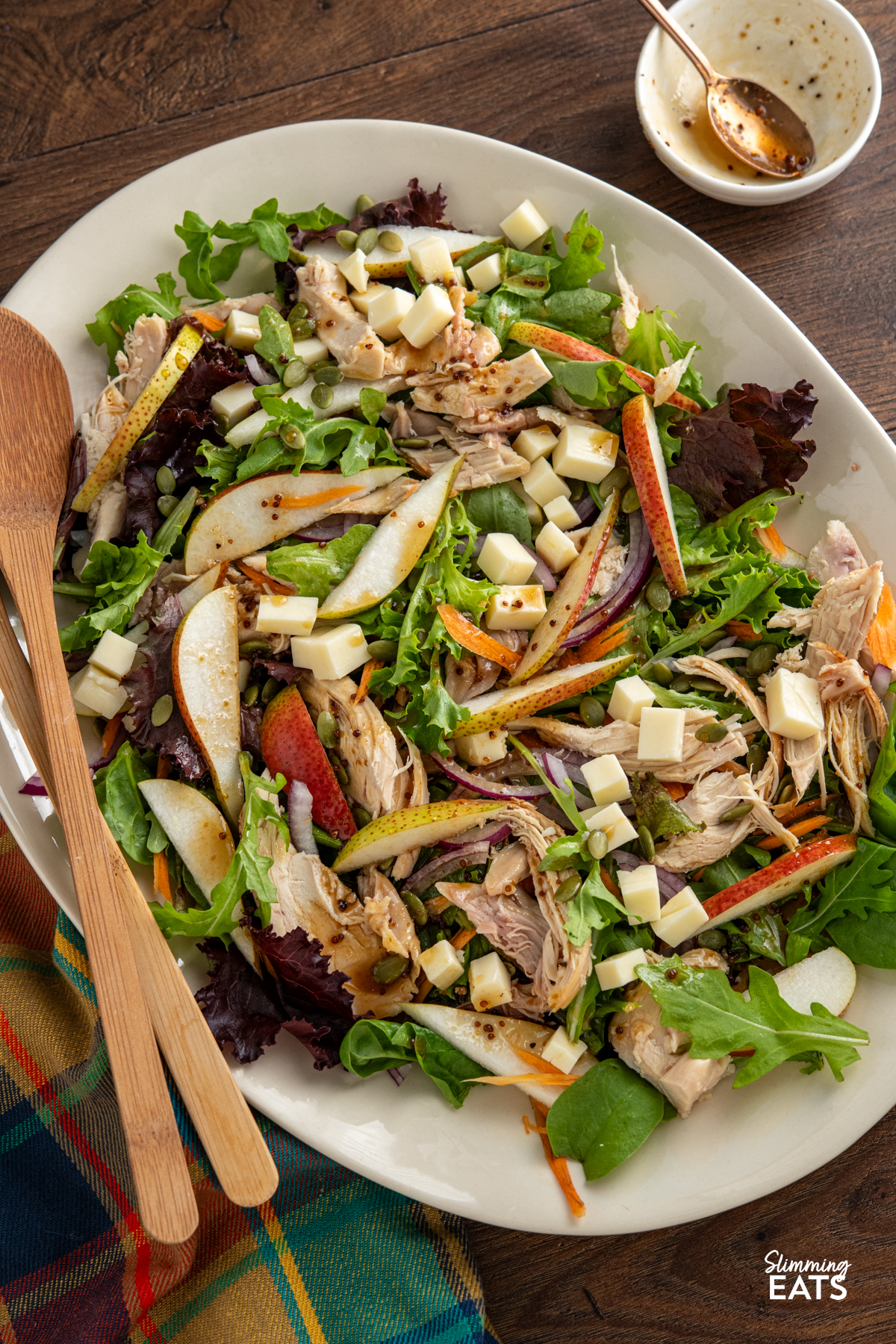 This Chicken Gouda Pear Salad is a delicious mix of sweet juicy pear, gouda, tender chicken, crunchy pumpkin seeds and baby greens, all tossed together with a mustard, lemon and maple dressing. It’s light, colourful and packed with flavour, while still being filling enough for lunch or dinner. Chicken, Gouda and Pear Salad on a oval beige plate with wooden salad spoons drizzled with dressing
