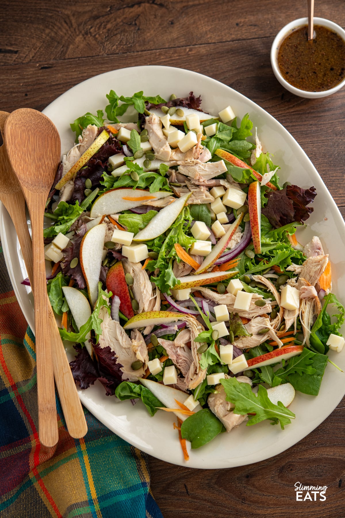 This Chicken Gouda Pear Salad is a delicious mix of sweet juicy pear, gouda, tender chicken, crunchy pumpkin seeds and baby greens, all tossed together with a mustard, lemon and maple dressing. It's light, colourful and packed with flavour, while still being filling enough for lunch or dinner. Chicken, Gouda and Pear Salad on a oval beige plate with wooden salad spoons
