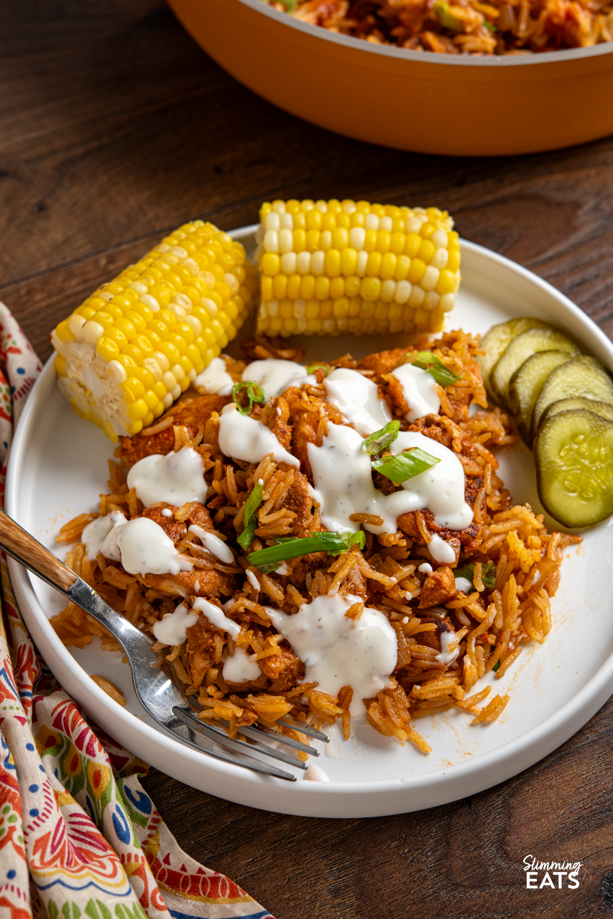 serving of One Pan Nashville Chicken and Rice on white plate drizzled with ranch and served with a side of corn on cob and pickles