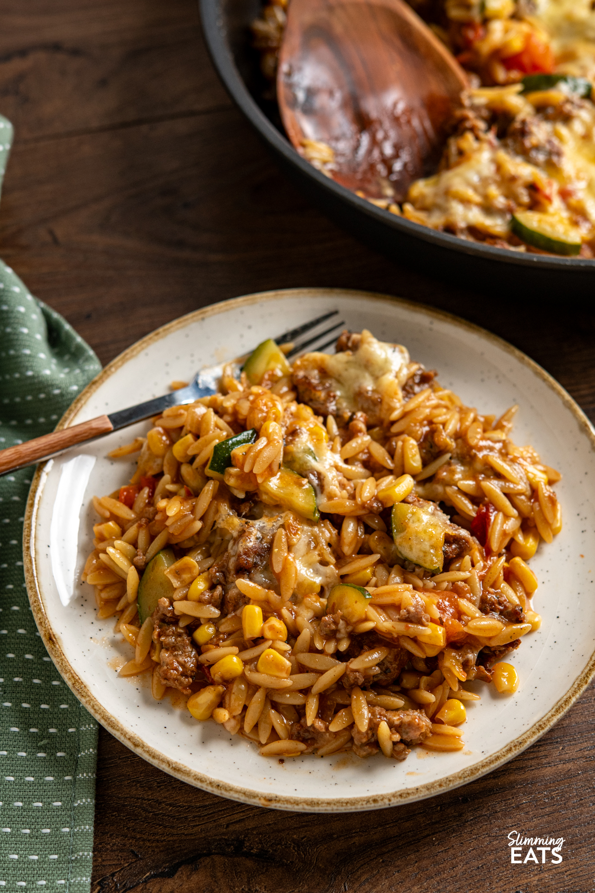 serving of Cheesy Ground Chicken Orzo with Zucchini and Corn one white plate with beige rim, fork with wooden style handle place on plate. 
